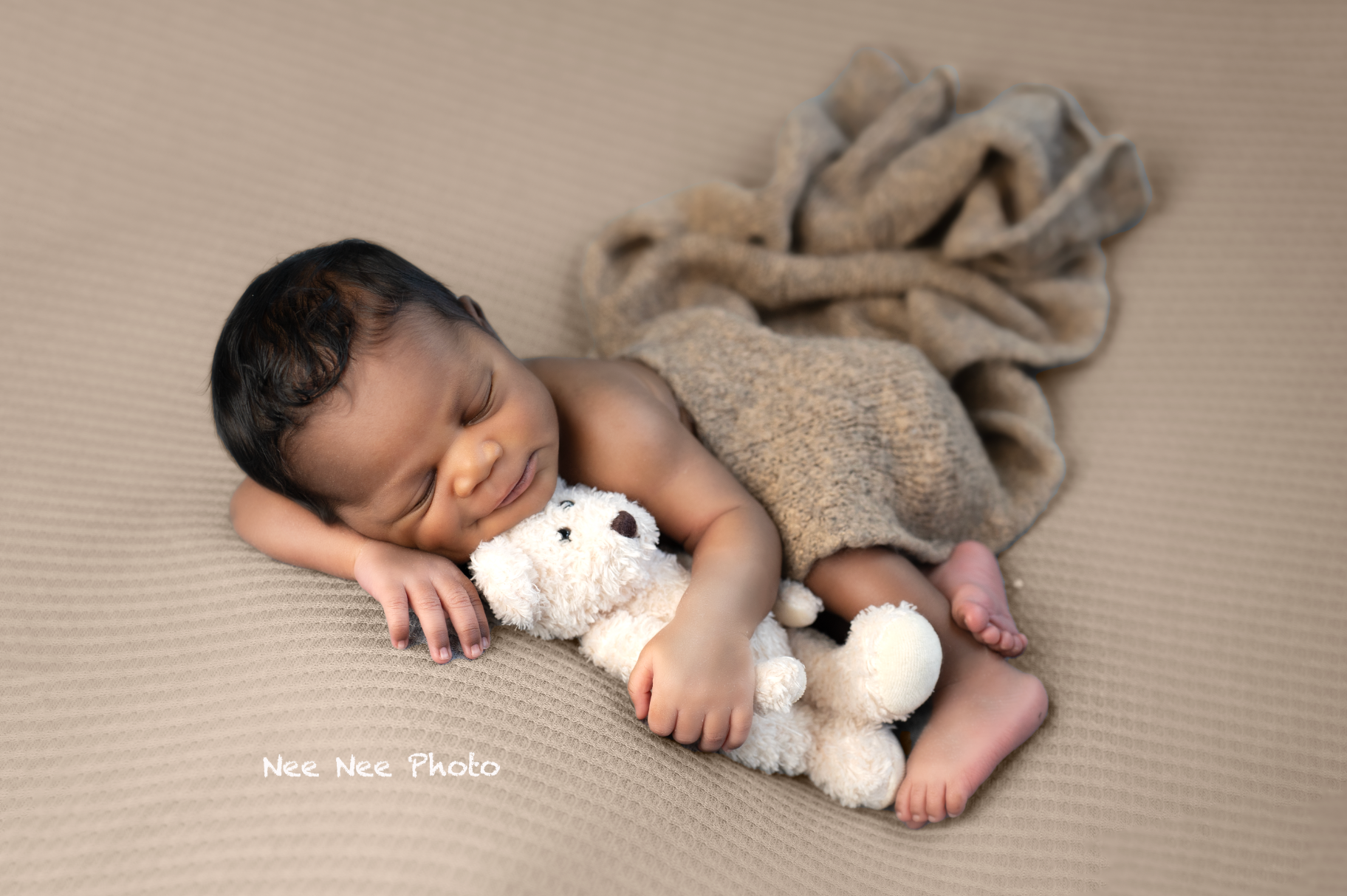 Newborn baby sleeping peacefully on tan blanket cuddling a small white stuffed animal toy in a professional photo. Embracing Life’s Beauty