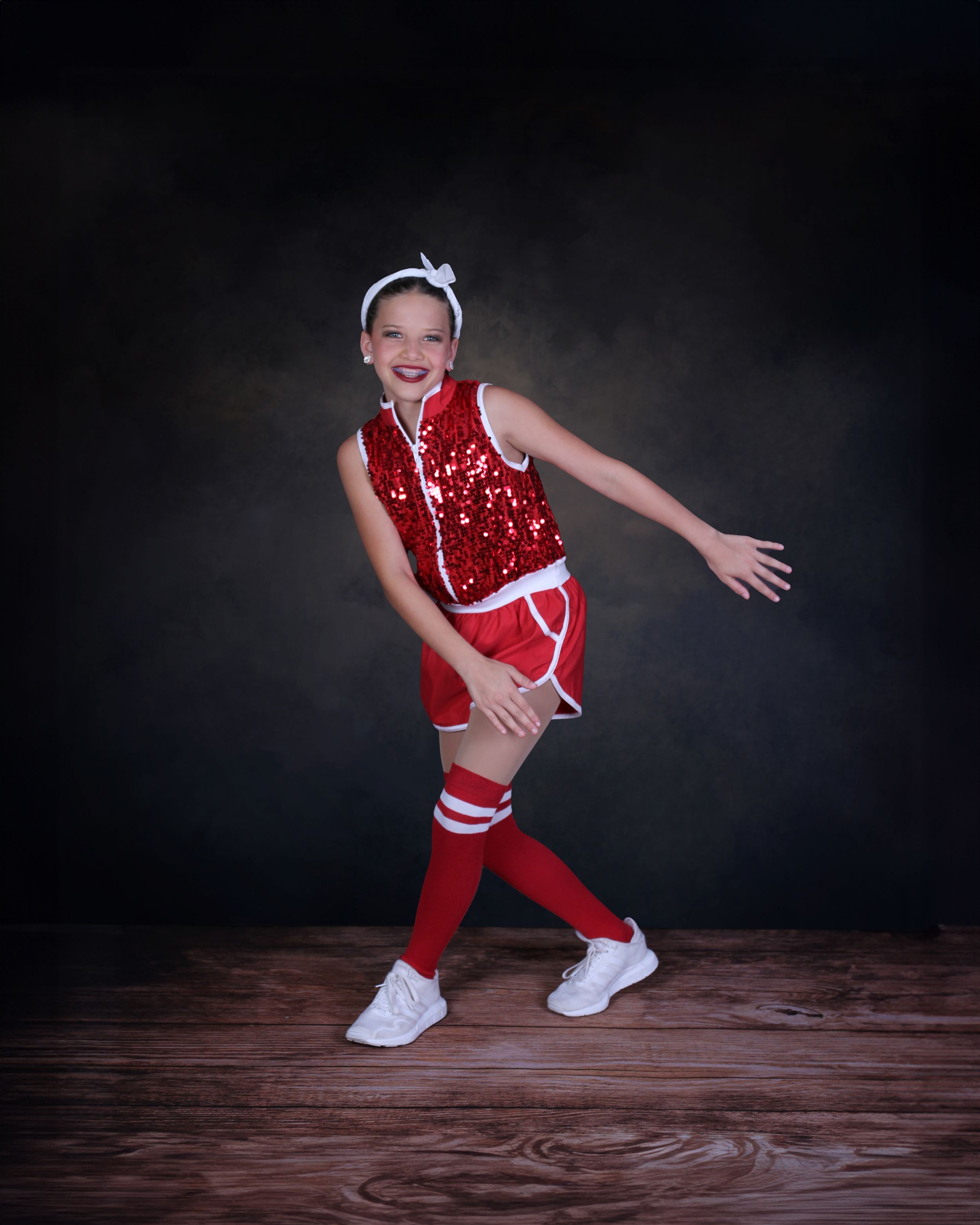 Dancer in red sequin costume strikes energetic pose on wooden floor.