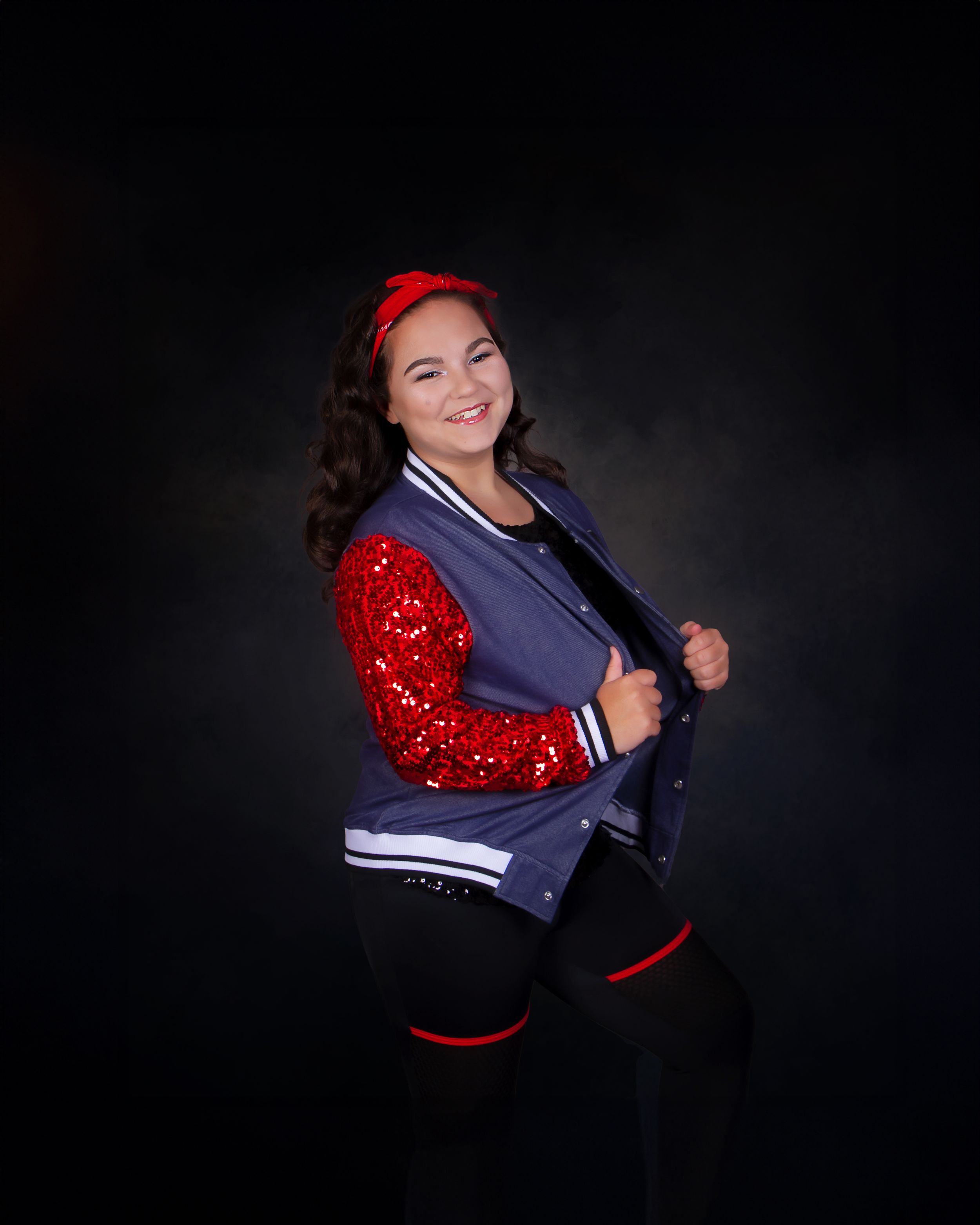 A student poses in a red and navy varsity letterman jacket against a dark studio backdrop.