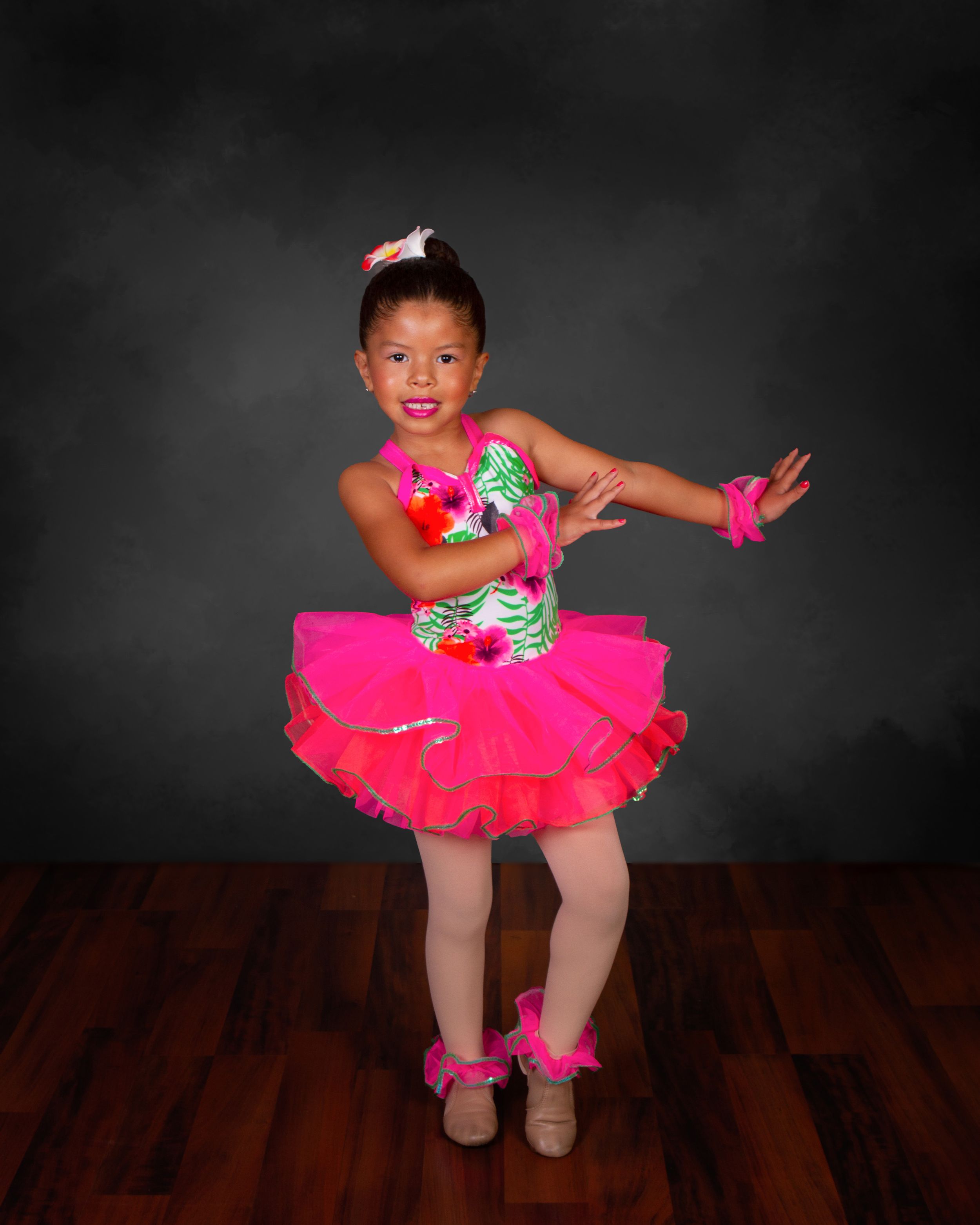 Dancer in bright pink tutu strikes playful pose against dark background.
