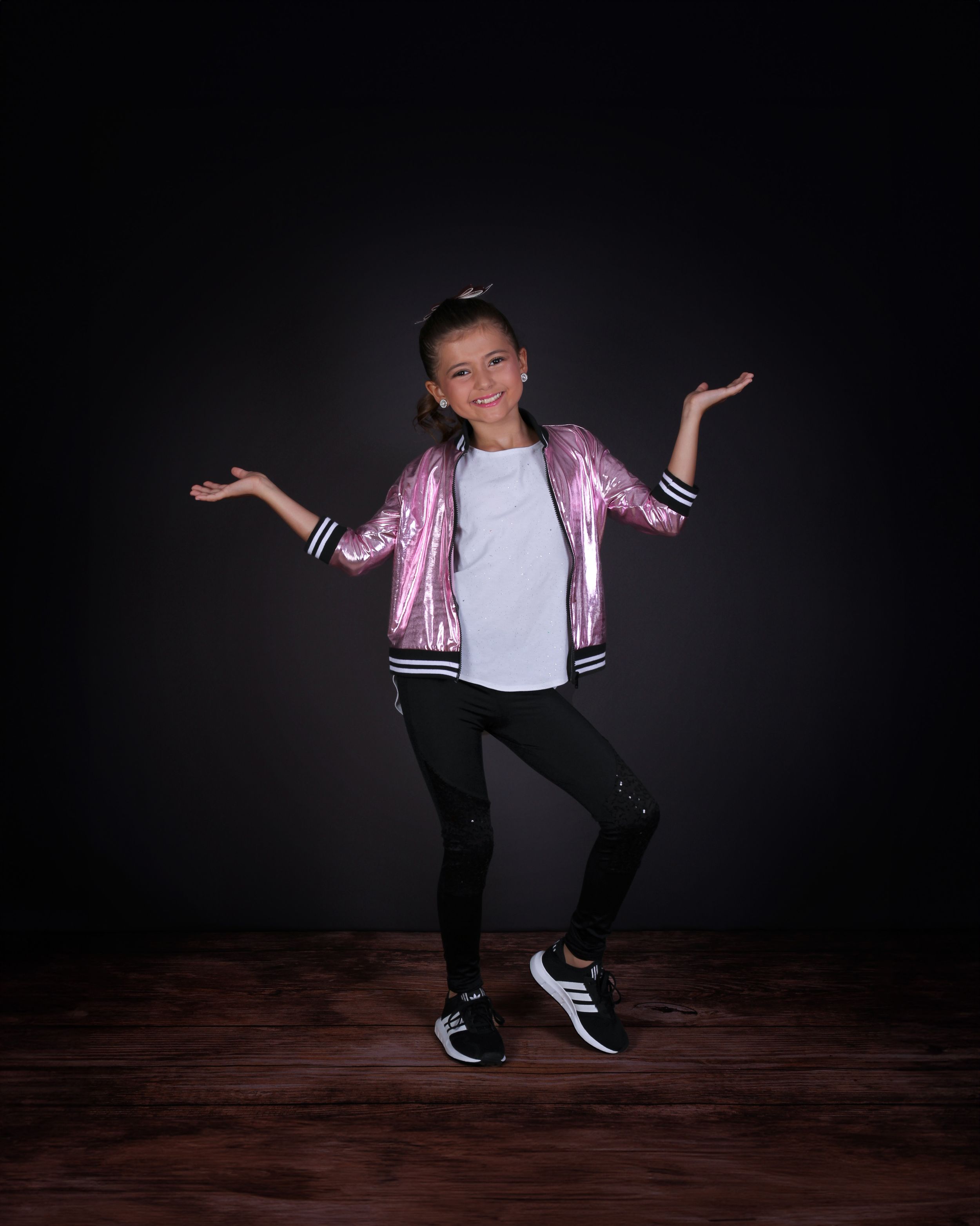 A dancer in a pink metallic jacket poses dynamically against a dark studio background.