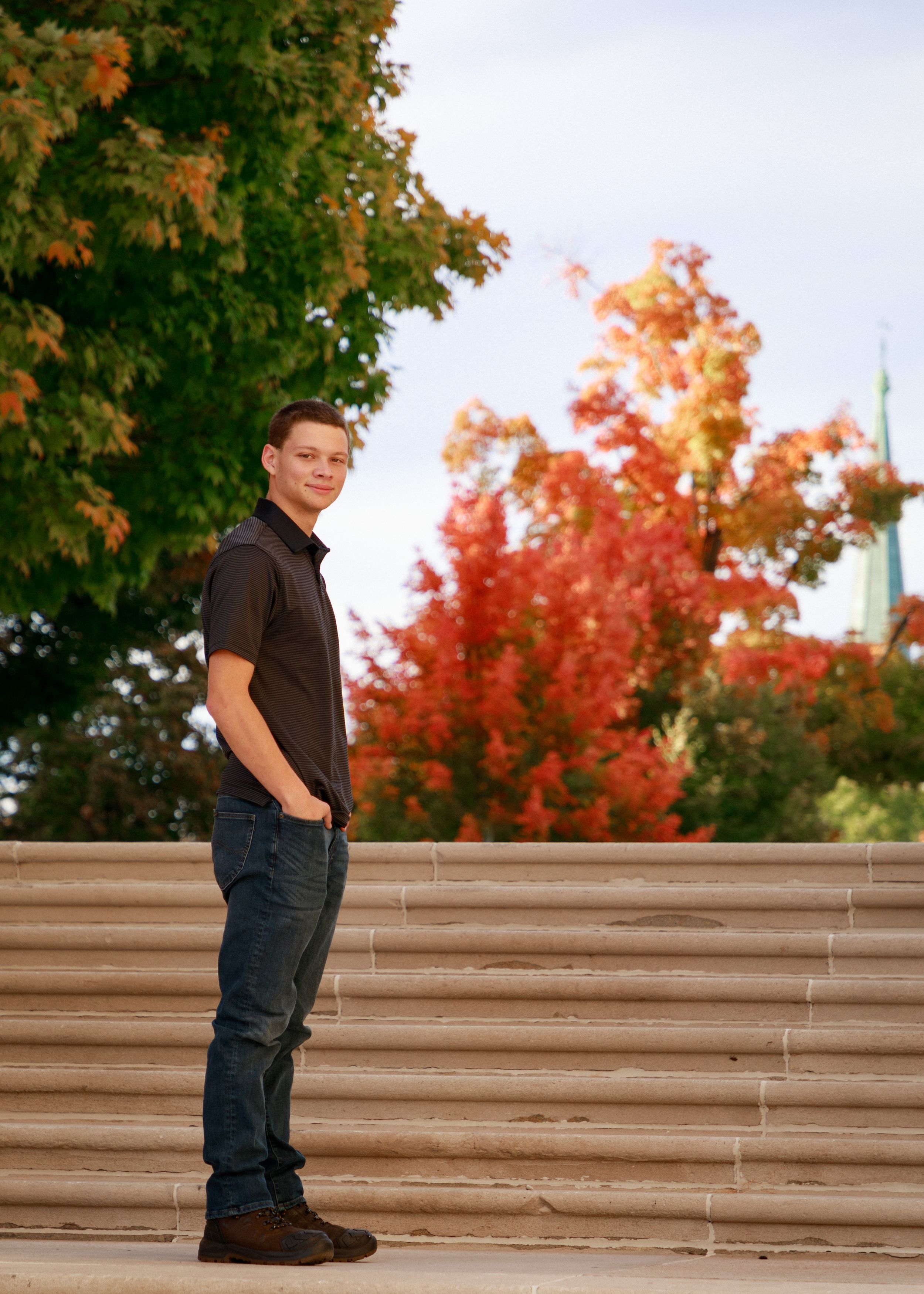 Autumn portrait on concrete steps with vibrant red maple trees in background.