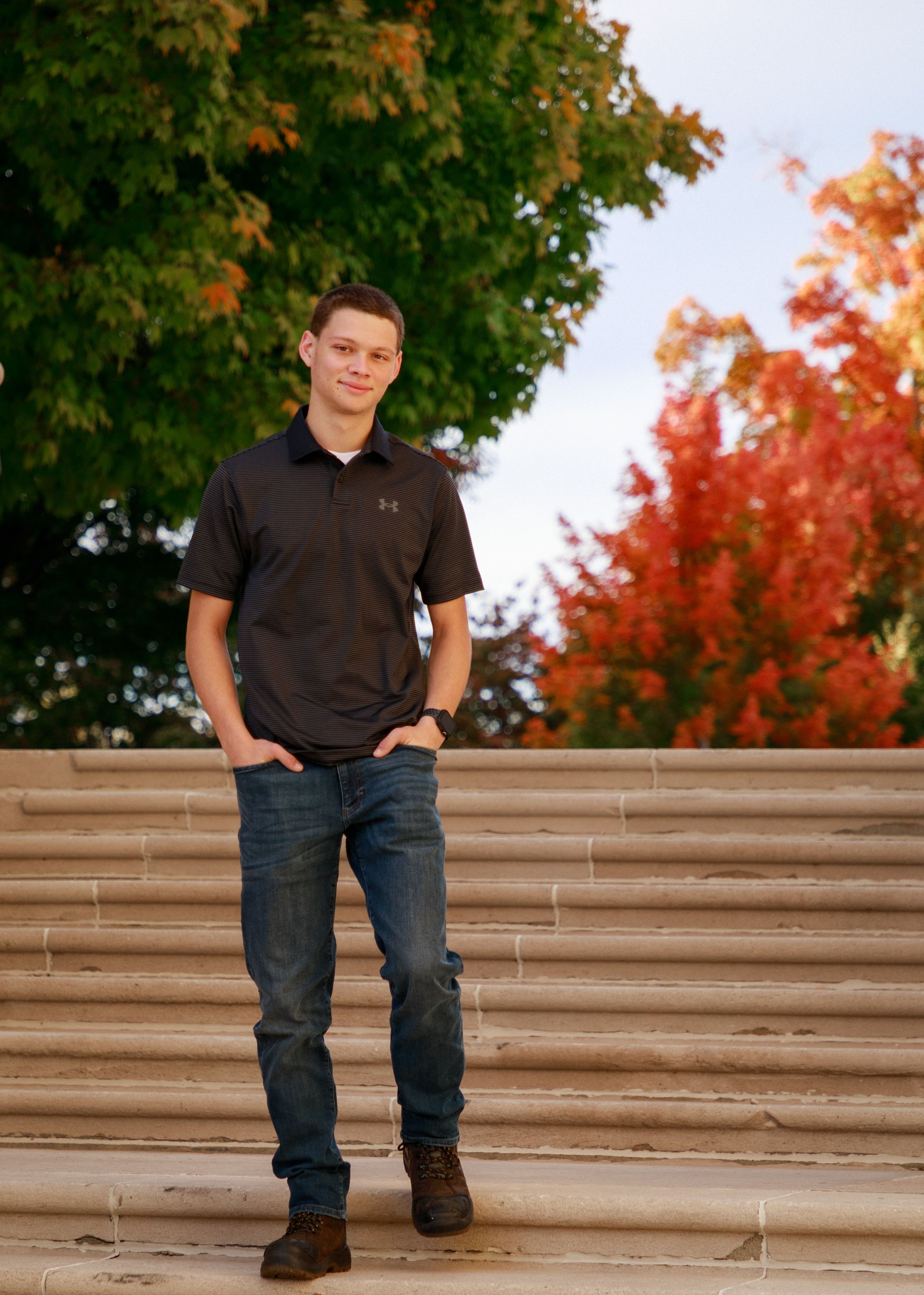 Portrait session on concrete steps with fall foliage creating colorful backdrop.