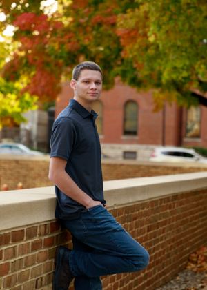 Person sitting on brick wall with colorful fall trees in background.