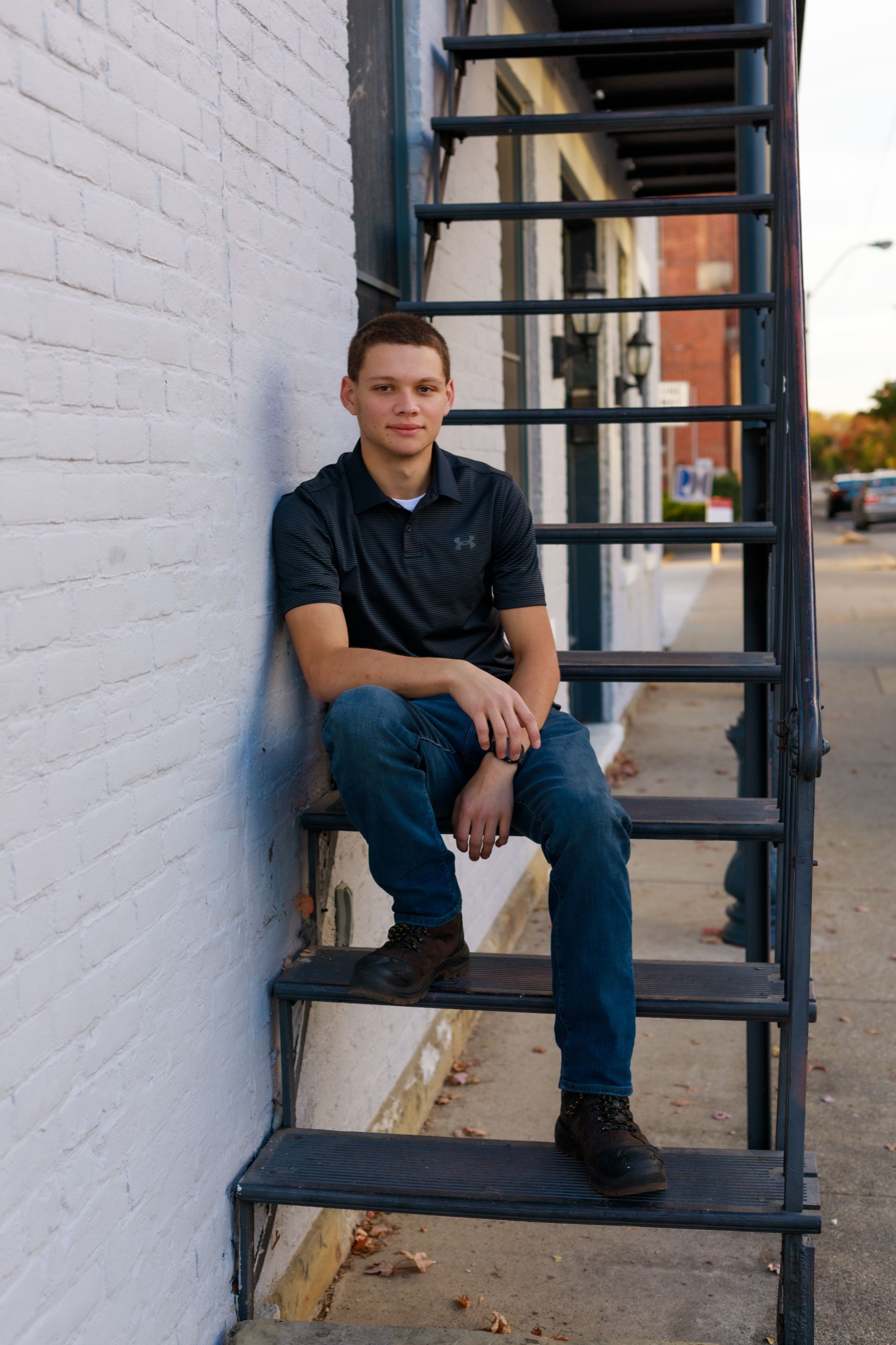 Person sitting on black metal stairs against white painted brick wall.