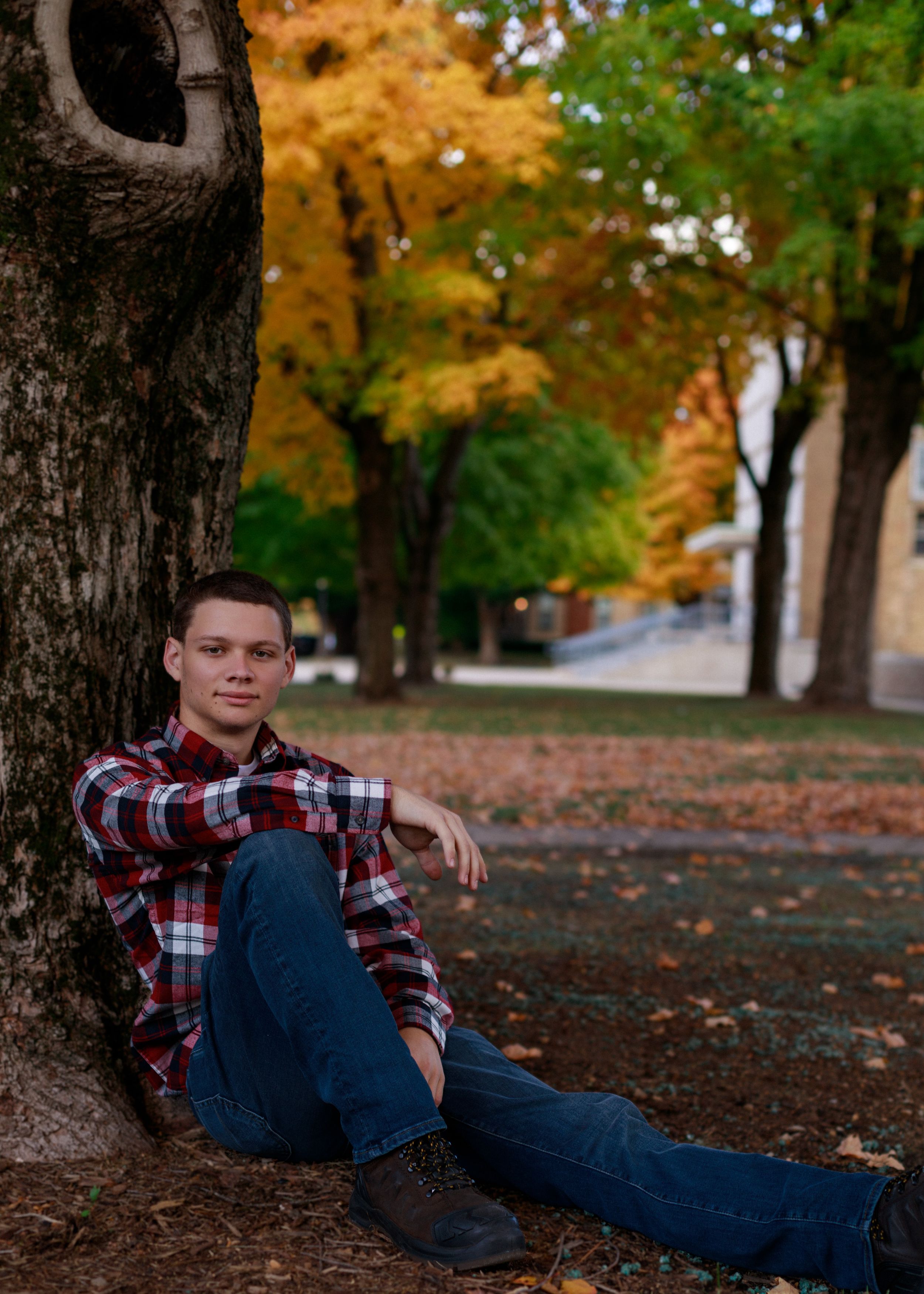 Person resting against tree in casual attire surrounded by colorful fall foliage.
