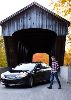 A rustic covered bridge with a black car parked inside during autumn.