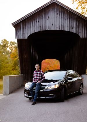 An old covered bridge with a car parked inside during autumn.