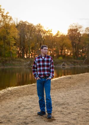 Person walking along lakeside beach during autumn sunset with trees in background.