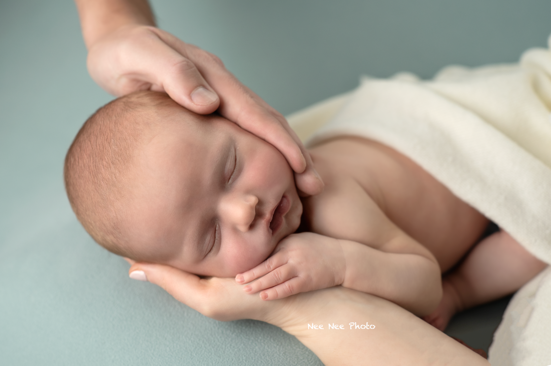 Sleeping newborn baby cradled in parent hands on teal background in professional studio photography. Embracing Life’s Beauty
