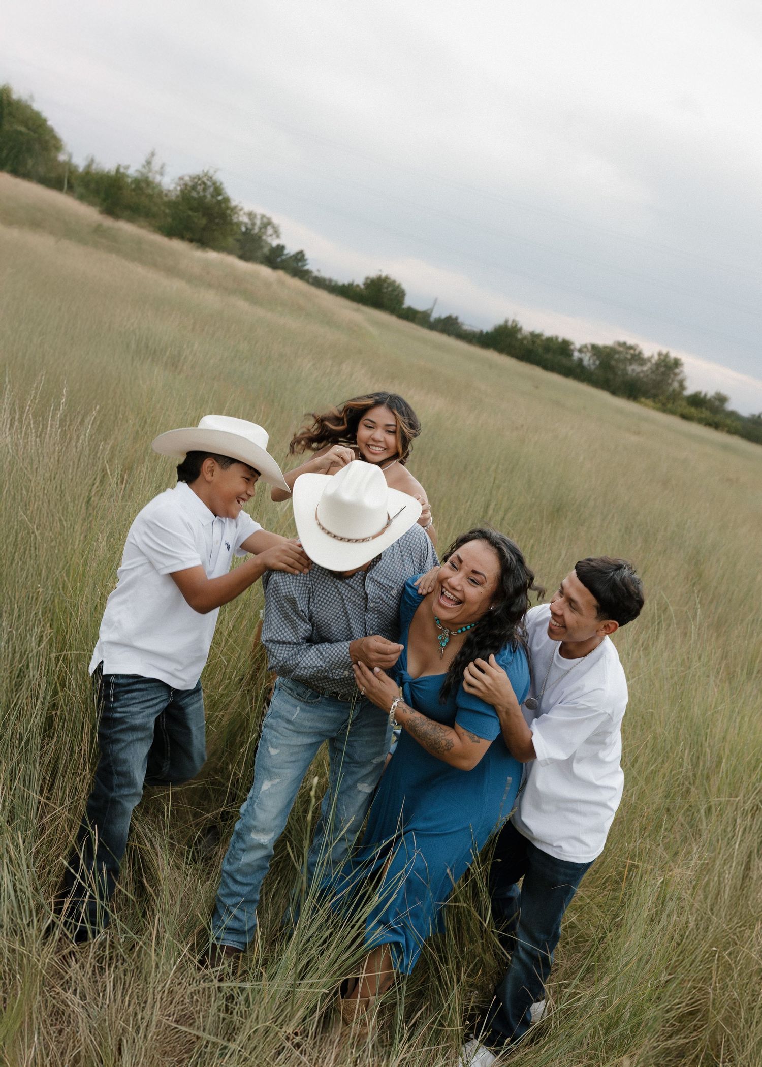 A family stands together in classic western attire on a rural field beneath dramatic stormy clouds.