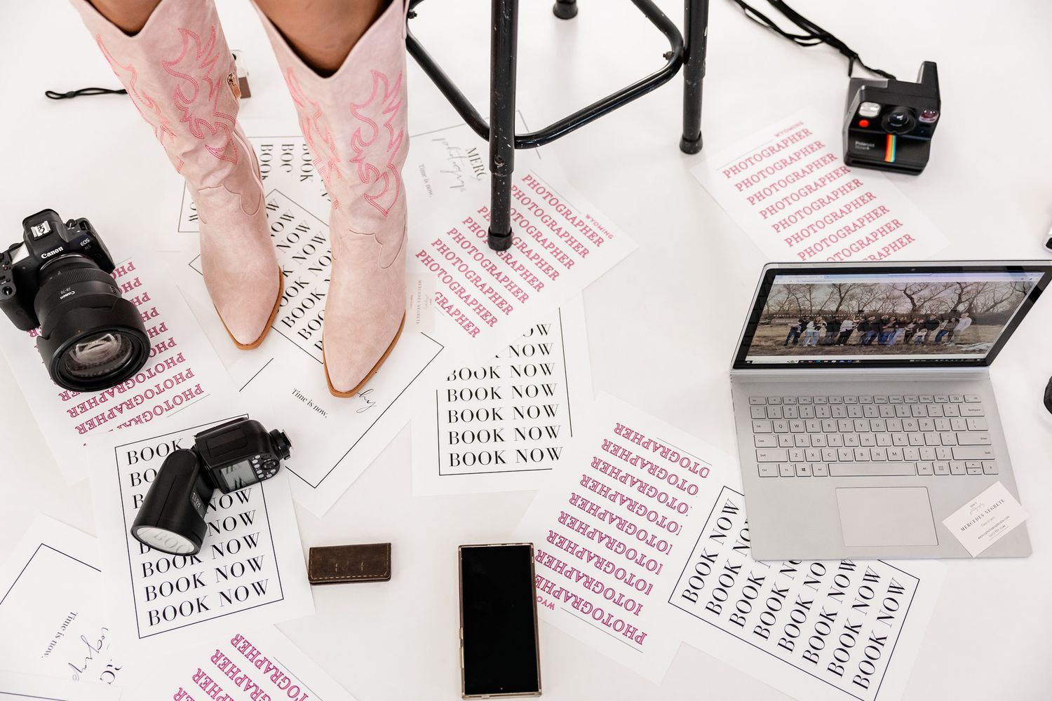 Wyoming Photographer
Flatlay workspace with pink cowboy boots, camera equipment, laptop and scattered papers with text on white background.