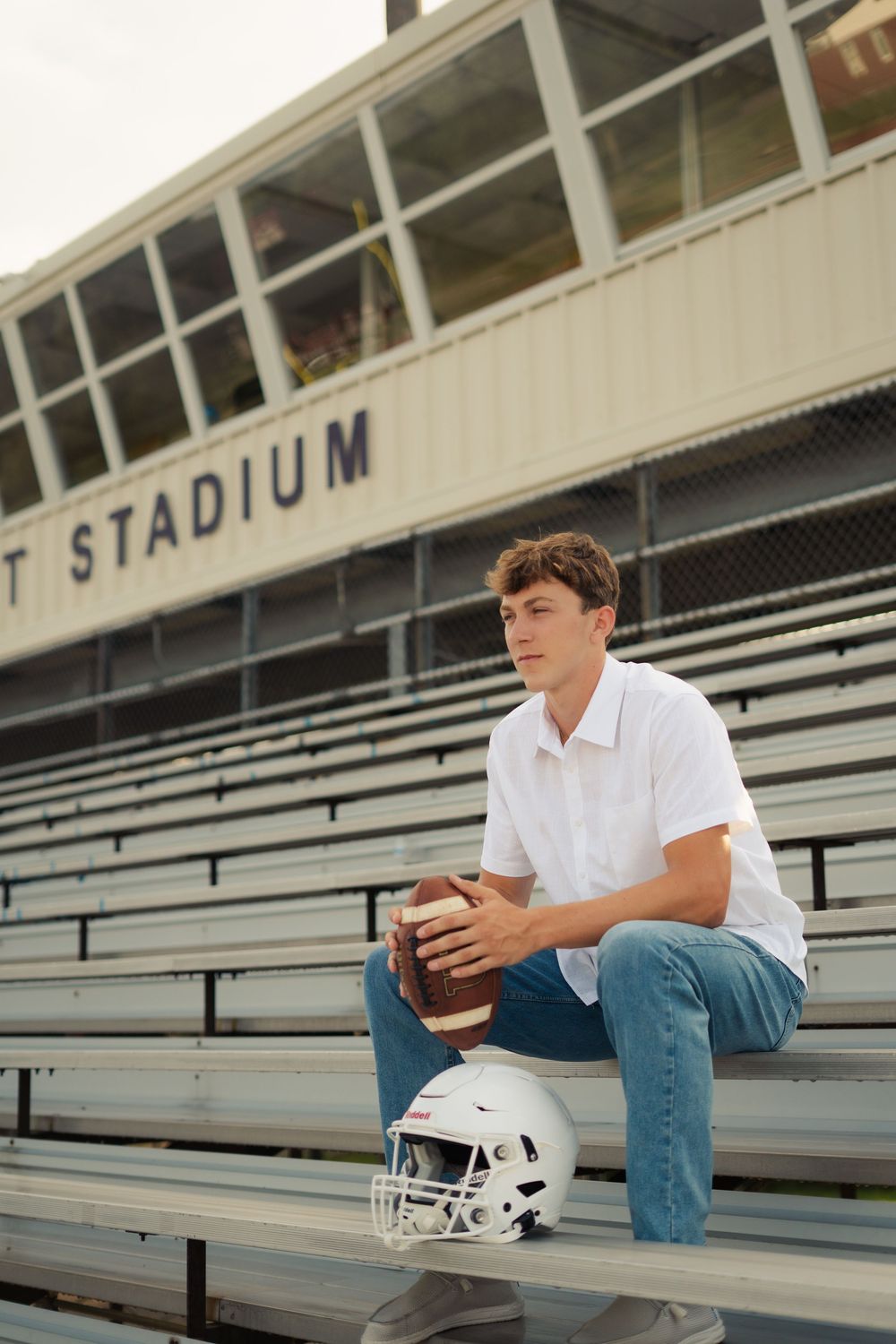 Student athlete sitting in empty stadium bleachers with football helmet.