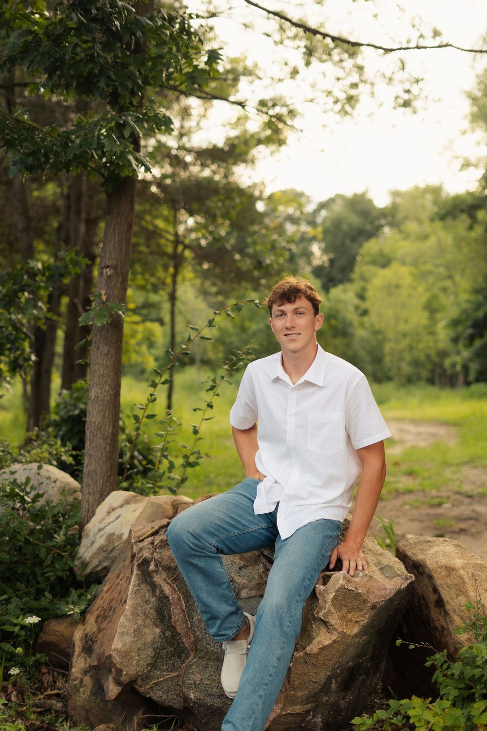 Senior portrait of student relaxing on natural rock formation in outdoor setting.
