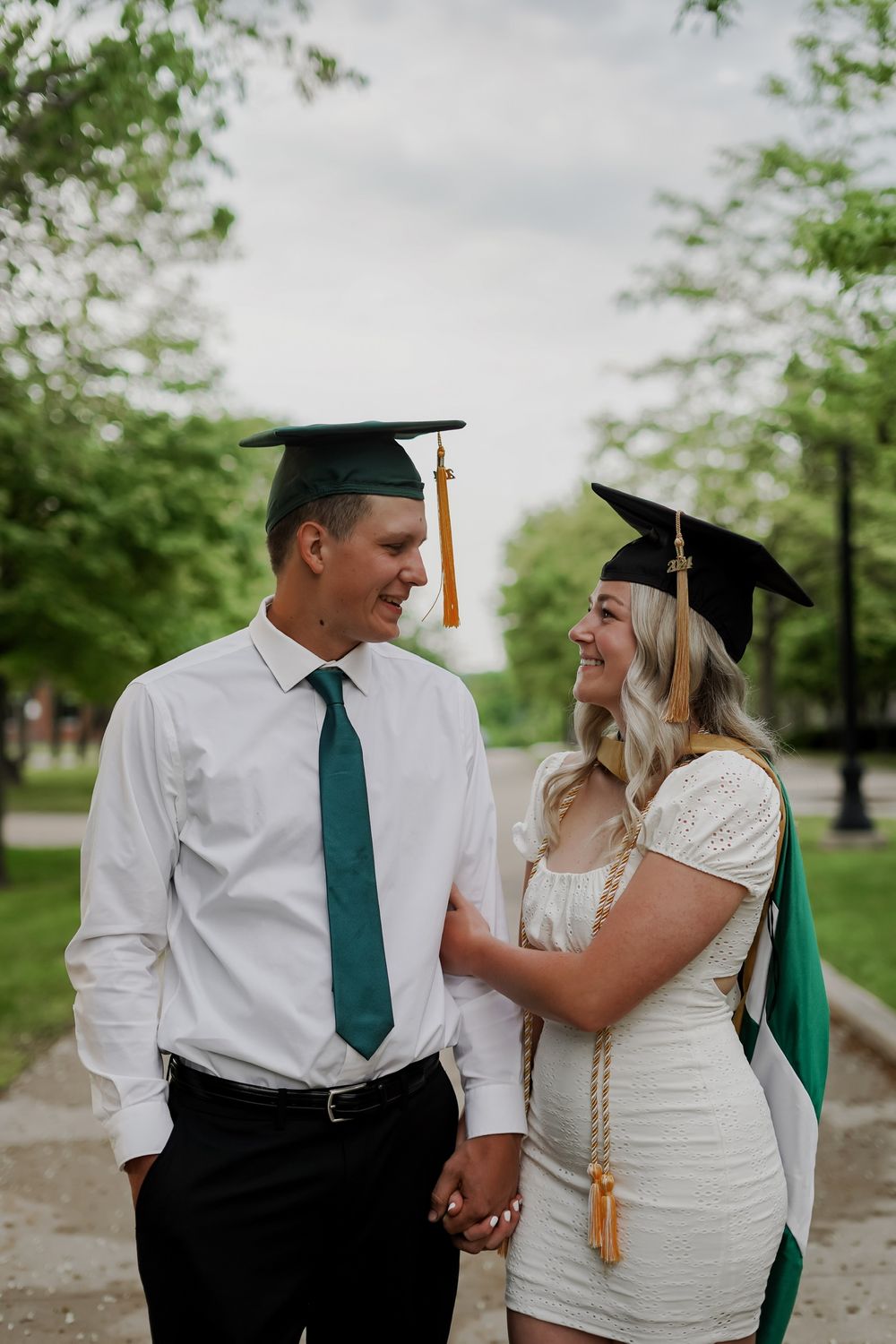 Graduates in formal attire and caps share celebratory moment on campus pathway.