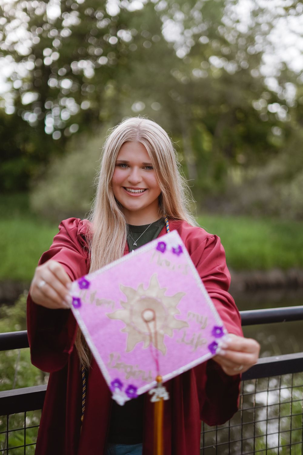 Person in burgundy jacket holding pink artwork on outdoor deck.
