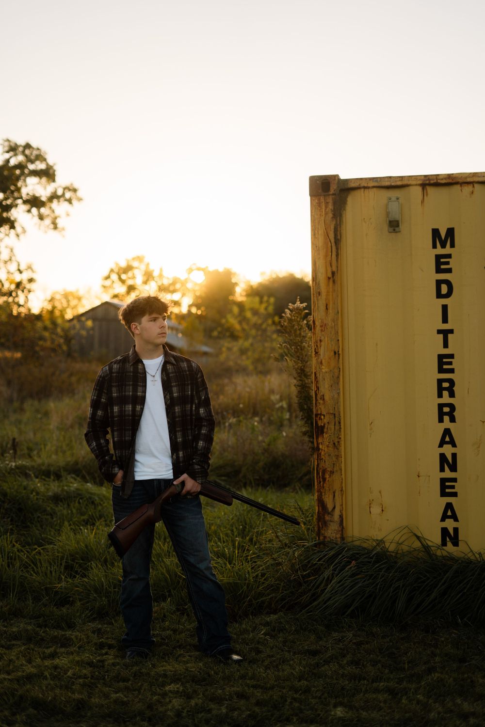 Young person poses near yellow storage containers at sunset wearing plaid jacket.