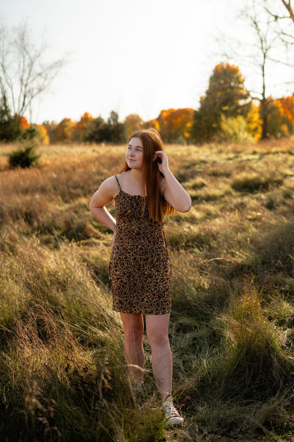 A person in a leopard print dress poses in tall grass during sunset.