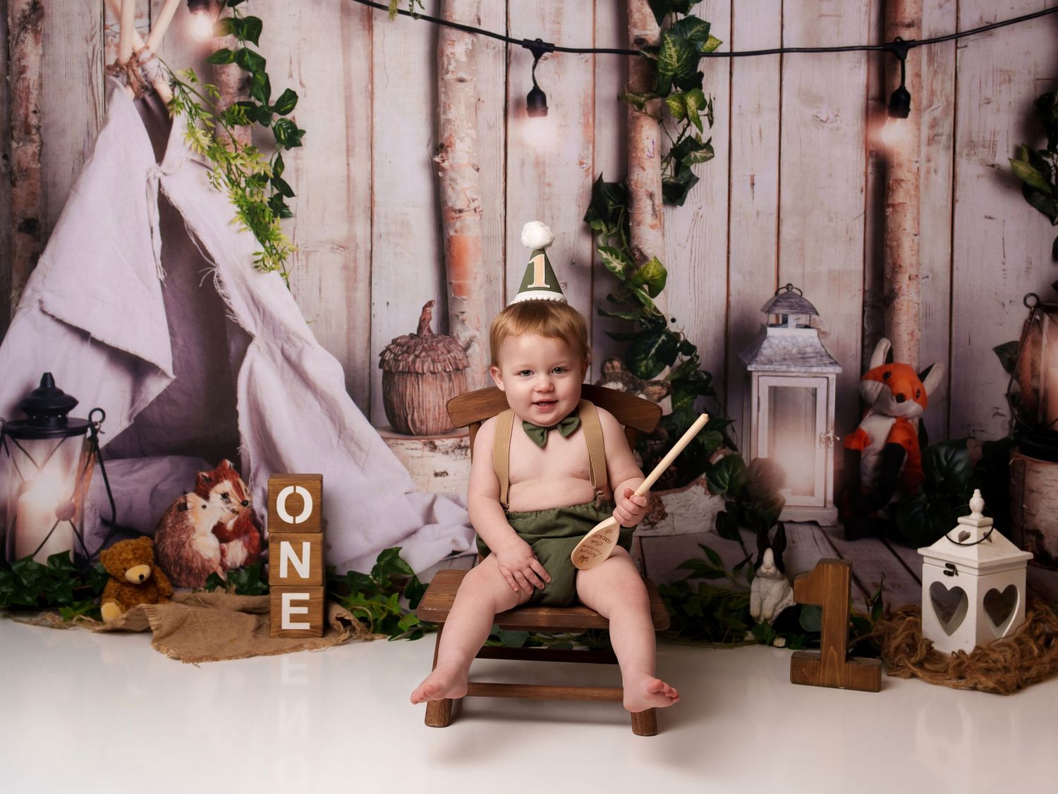 Baby sitting in rustic themed set with teepee, lanterns and woodland decorations.