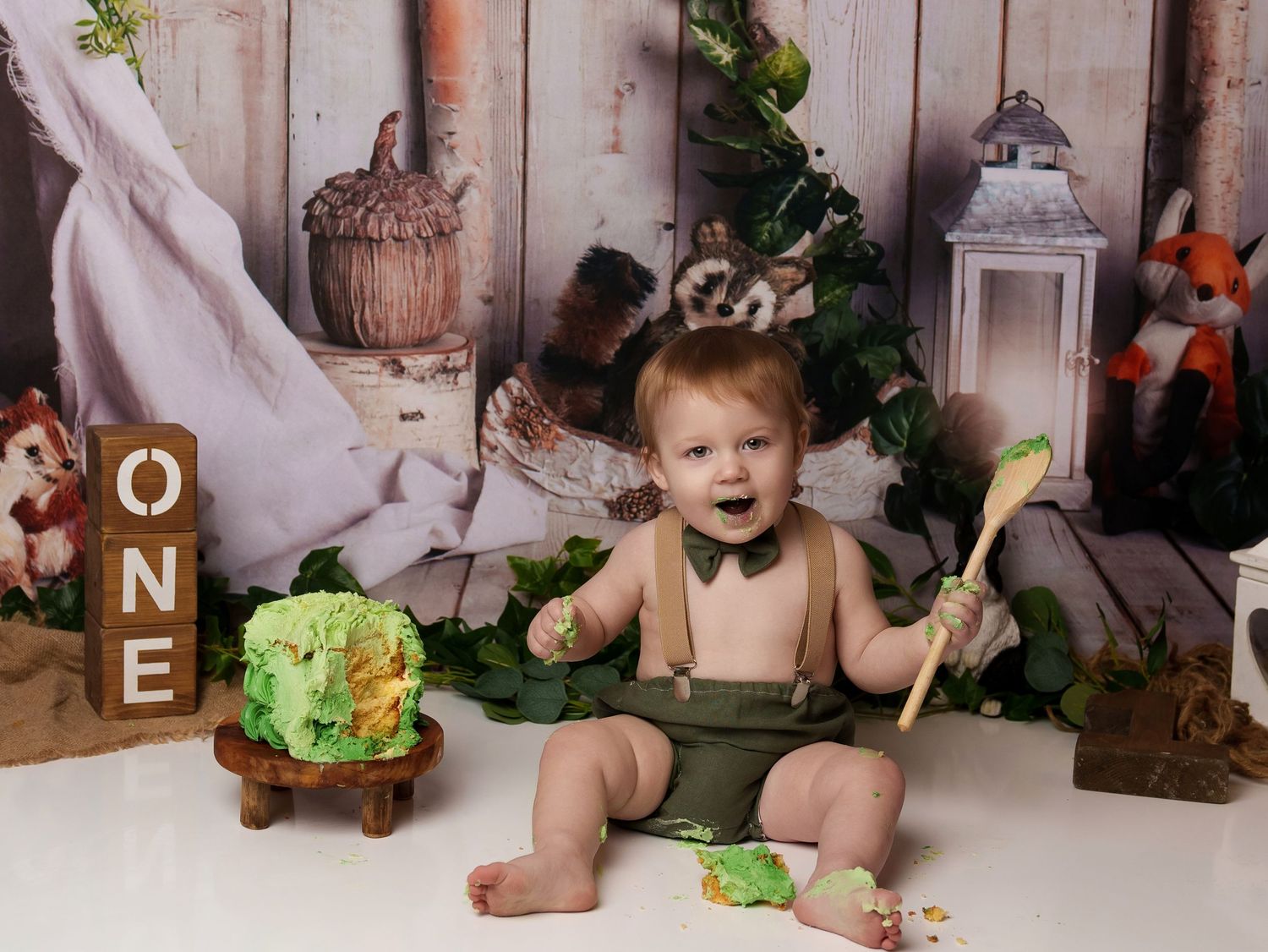 Woodland-themed first birthday setup with rustic decorations and a green smash cake.
