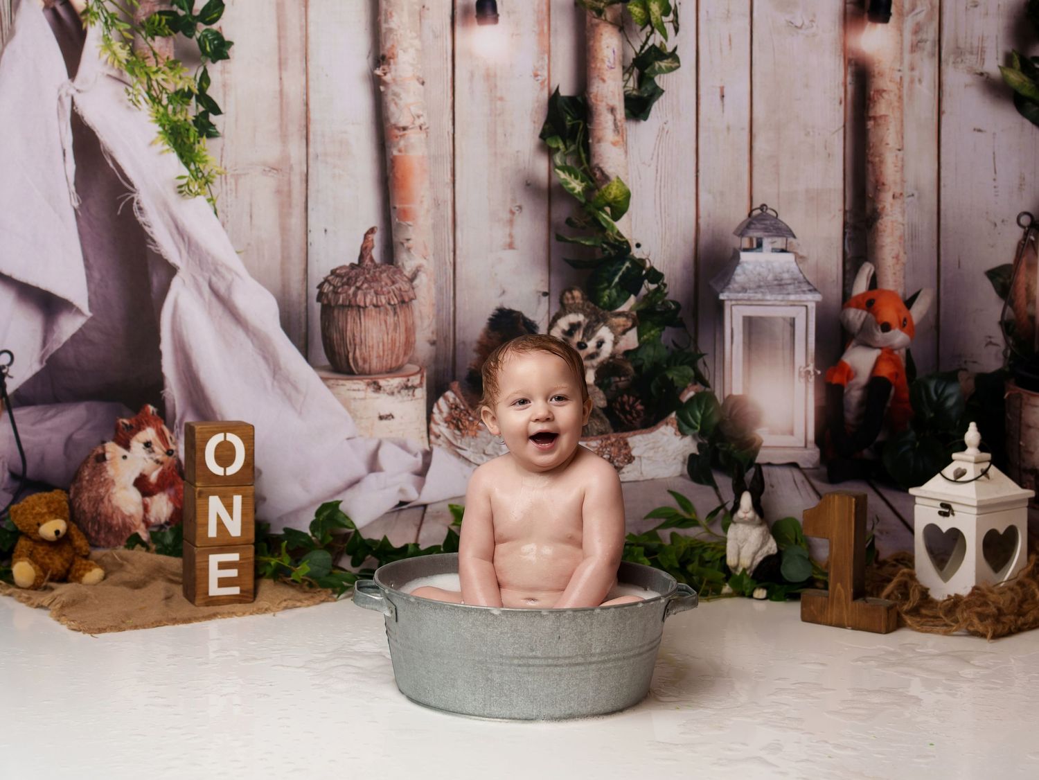 Rustic first birthday setup with metal tub, lanterns, and woodland animal decorations.