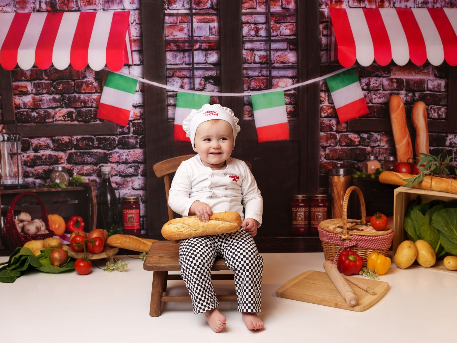 Little chef photoshoot with Italian market backdrop, fresh produce, and hanging flags.