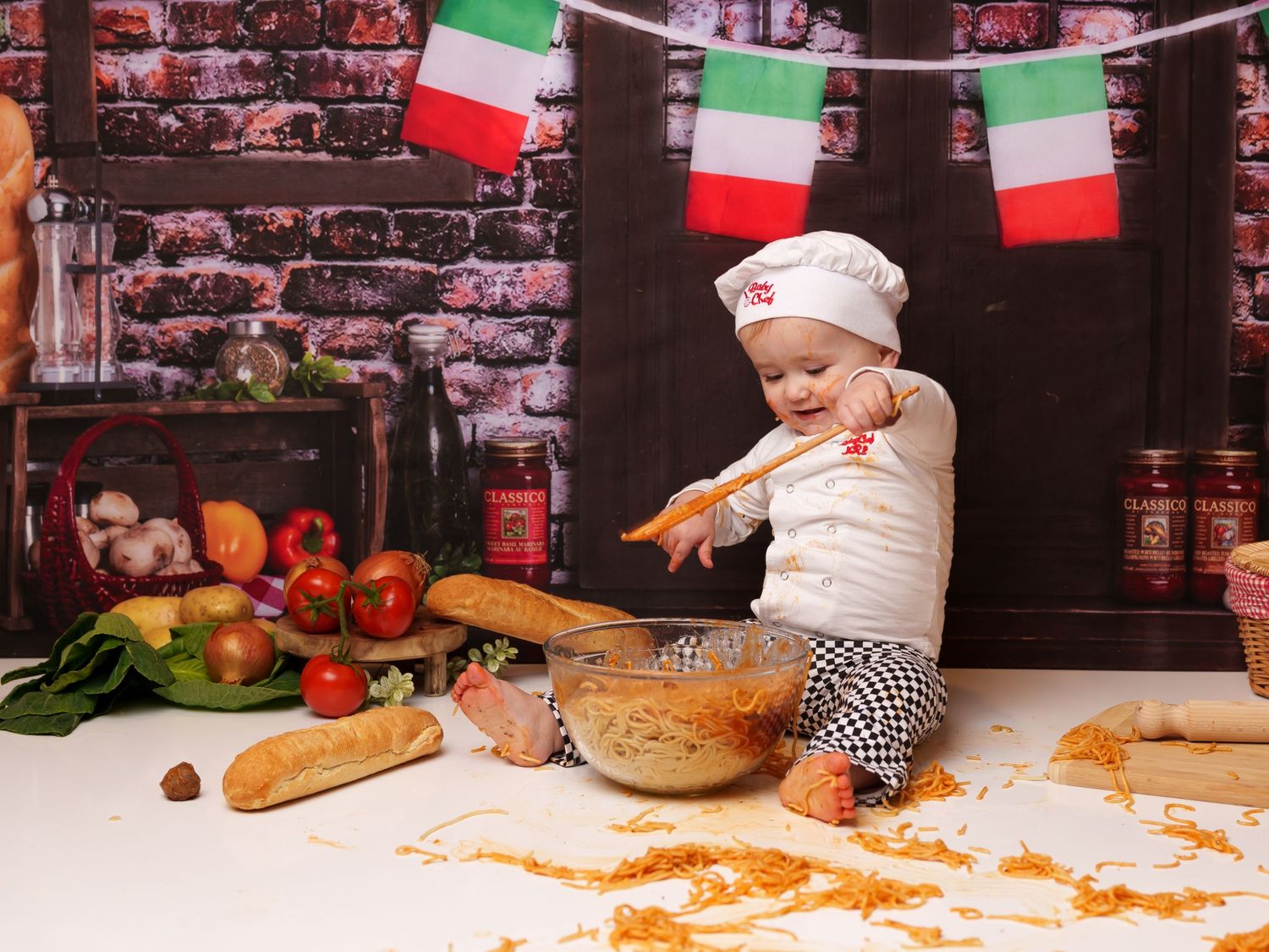 Italian cooking themed photoshoot with messy spaghetti and market backdrop.