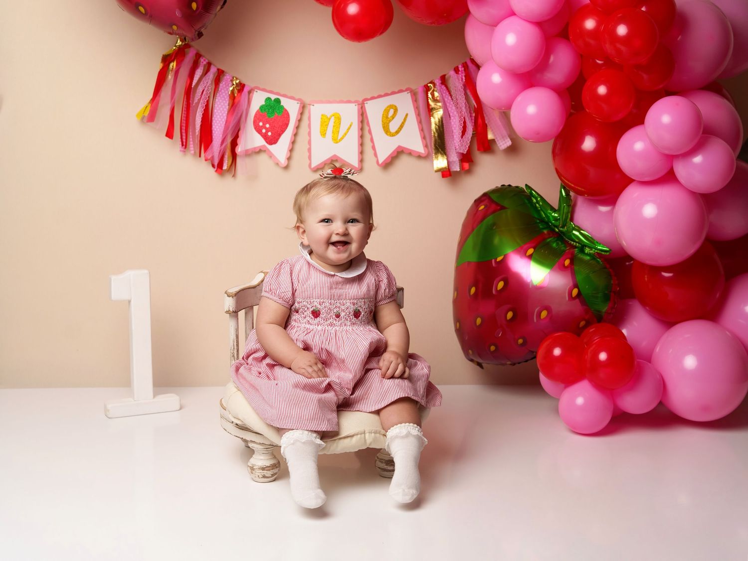 First birthday celebration setup with pink balloons and large strawberry decoration.
