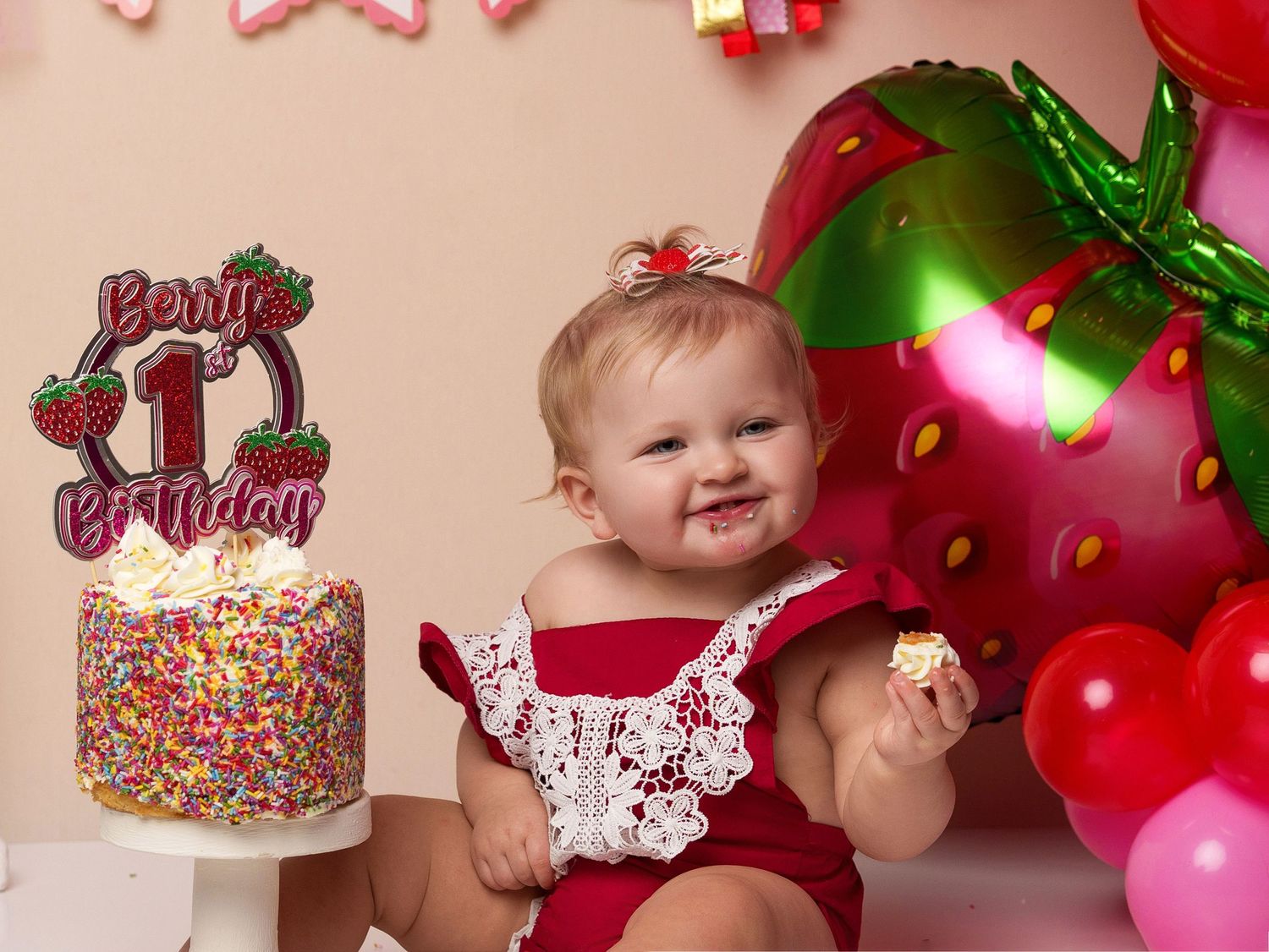 Strawberry-themed first birthday party with sprinkle cake and balloon arch.
