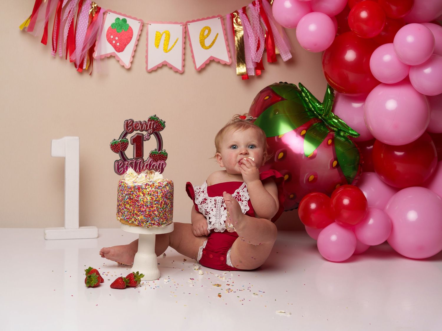 Pink and red strawberry-themed cake smash setup with sprinkle decorations.