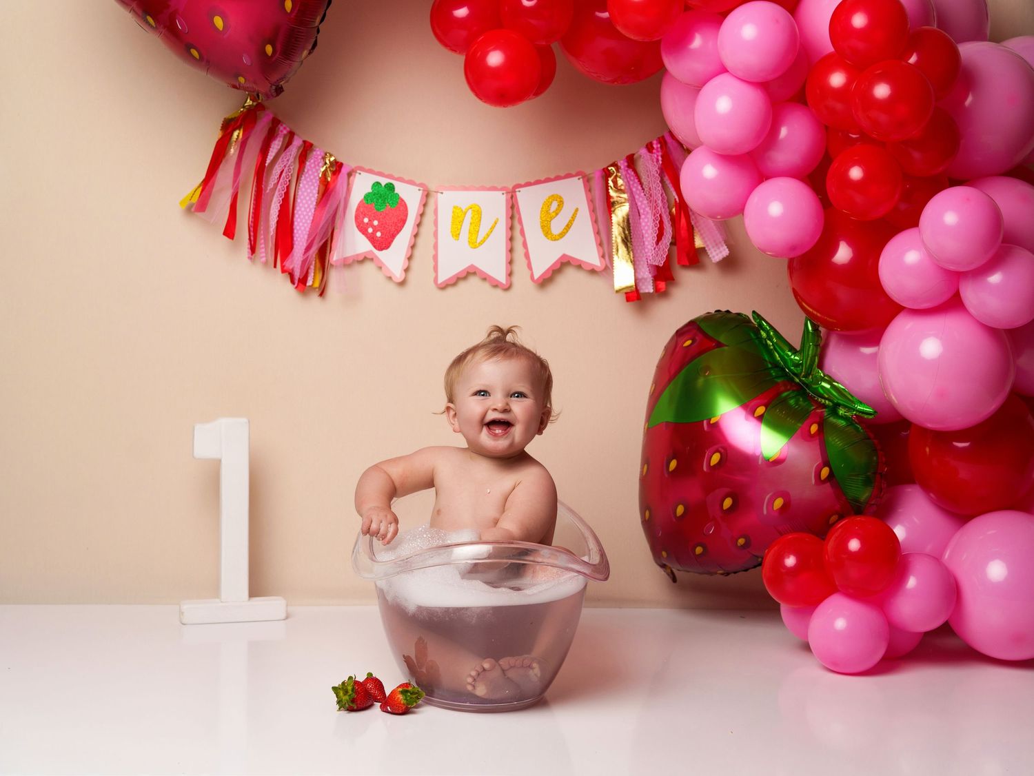 First birthday cake smash with pink balloons and metallic strawberry decorations.