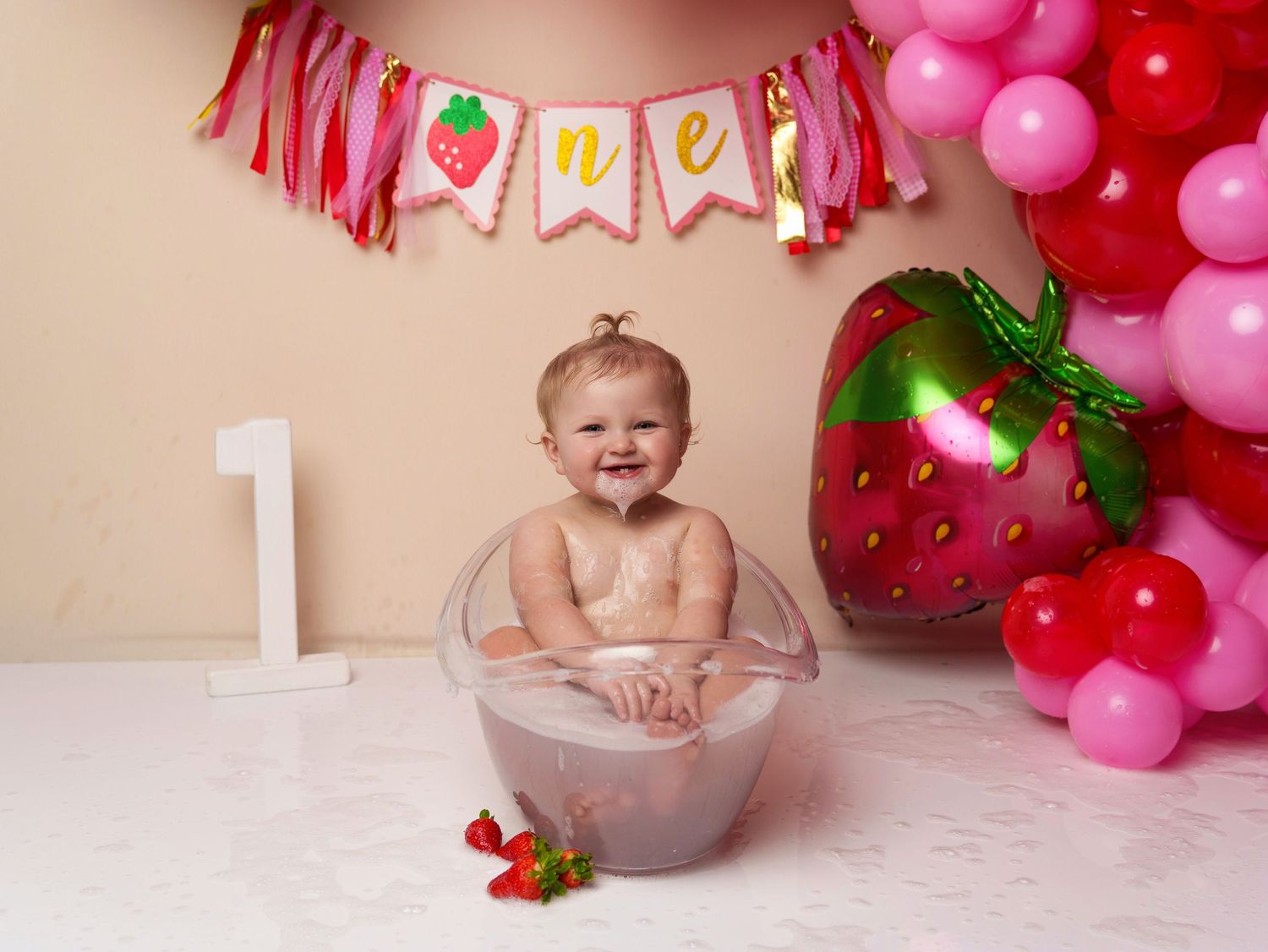 First birthday celebration setup with pink decorations, a large strawberry prop, and pink balloons.
