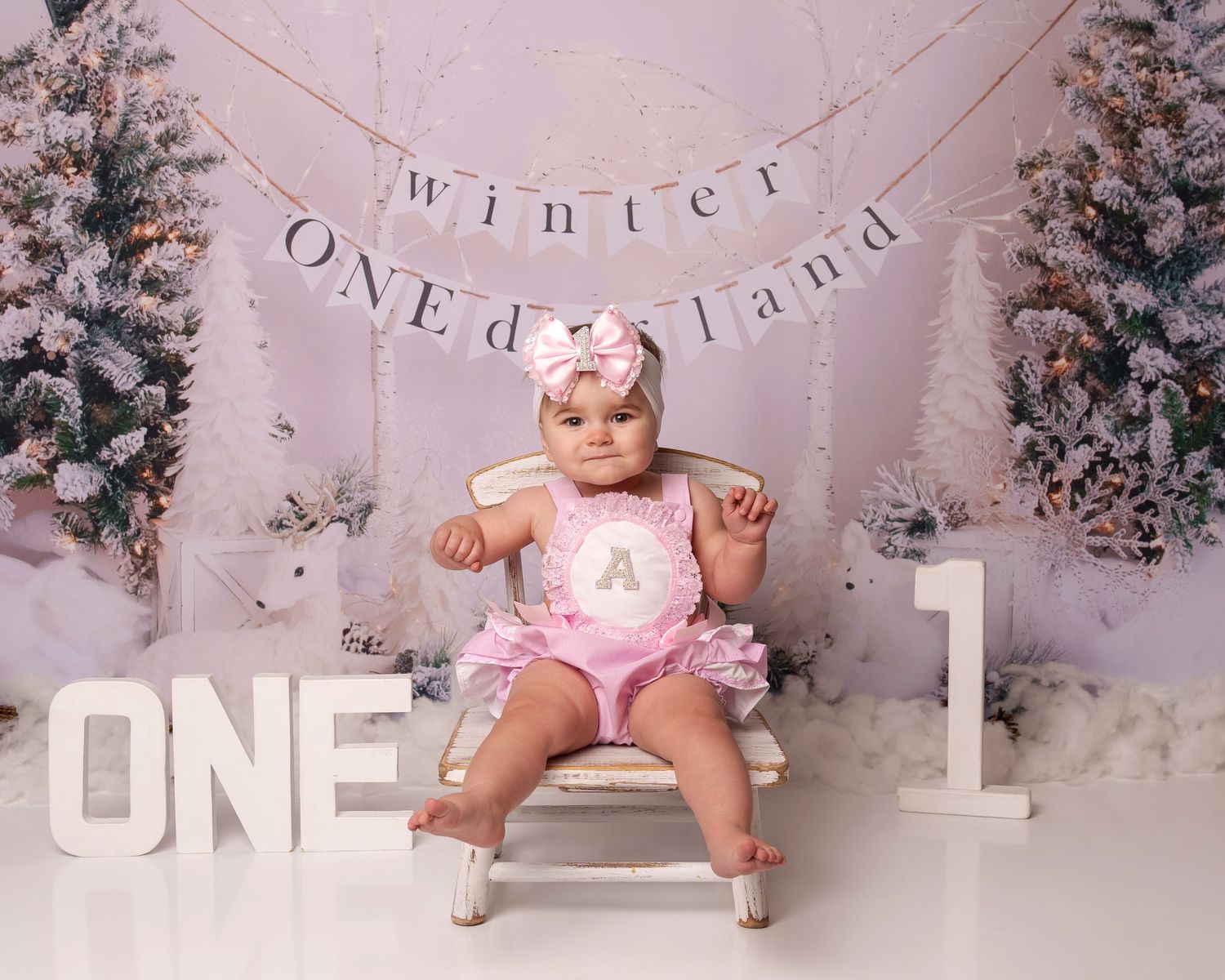 Winter wonderland themed first birthday setup with snowy trees and letter banner decorations.