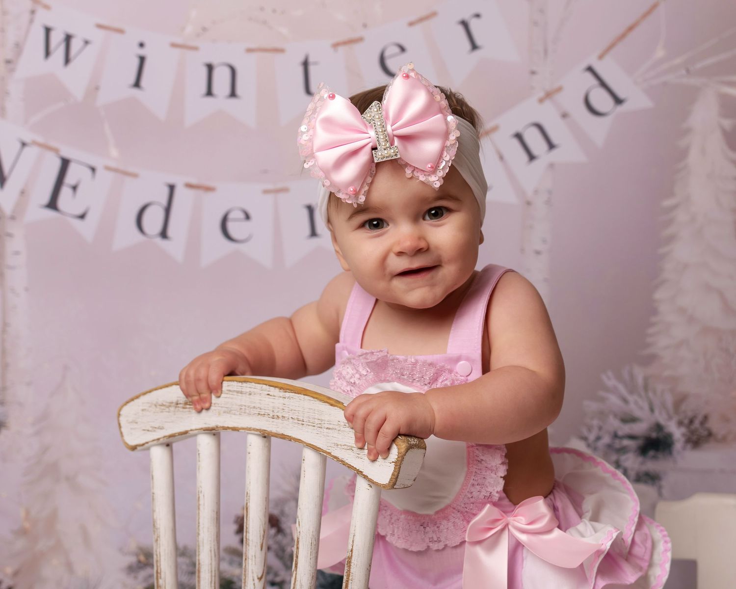 Pink winter wonderland themed photo setup with white chair and decorative banner.