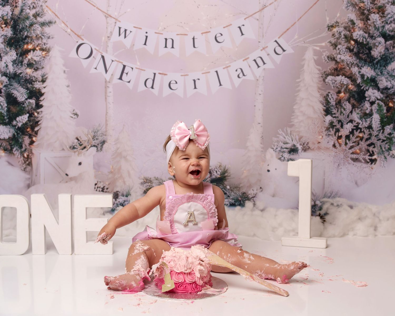 Winter wonderland cake smash scene with pink dress and snowy decorations.
