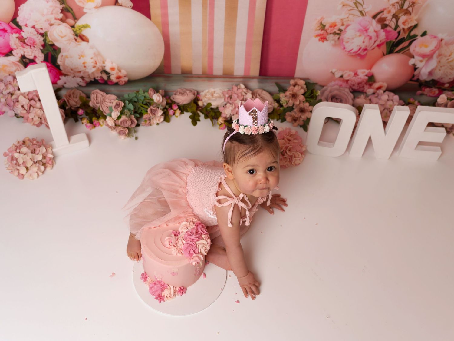 Pink and white first birthday party setup with decorative balloons, flowers and text reading ONE.