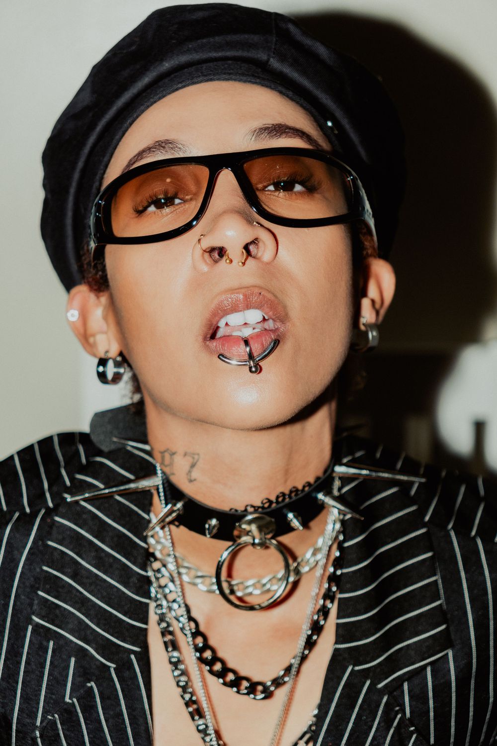 Edgy portrait with black beret, glasses, striped jacket and layered chain accessories.