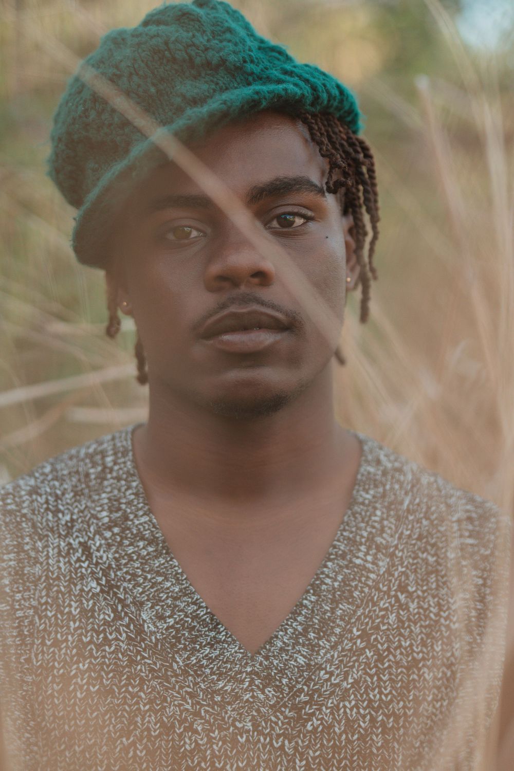 Artistic portrait of someone wearing a teal beanie and V-neck sweater against a dreamy natural backdrop.
