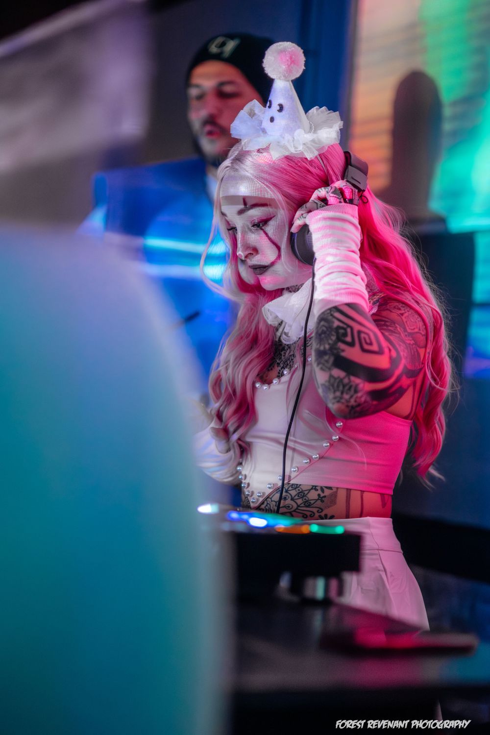 A performer in white costume illuminated by colorful stage lighting during a show.