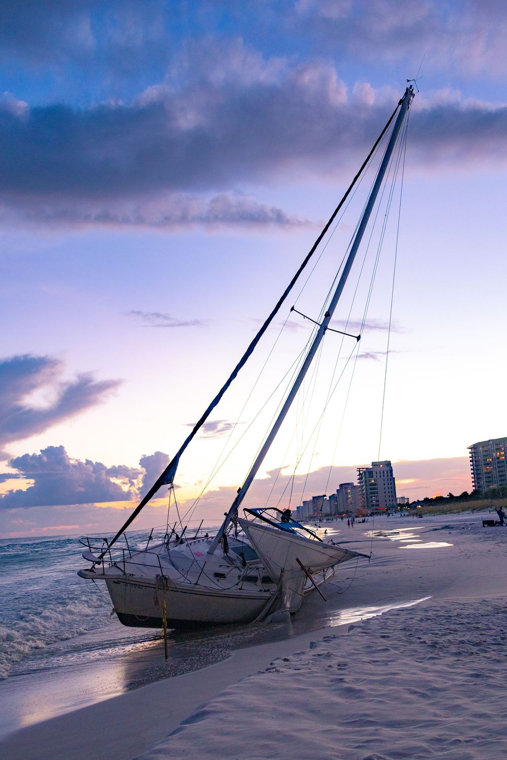 Sailboats stranded on a beach during low tide at sunset with colorful clouds in the background.