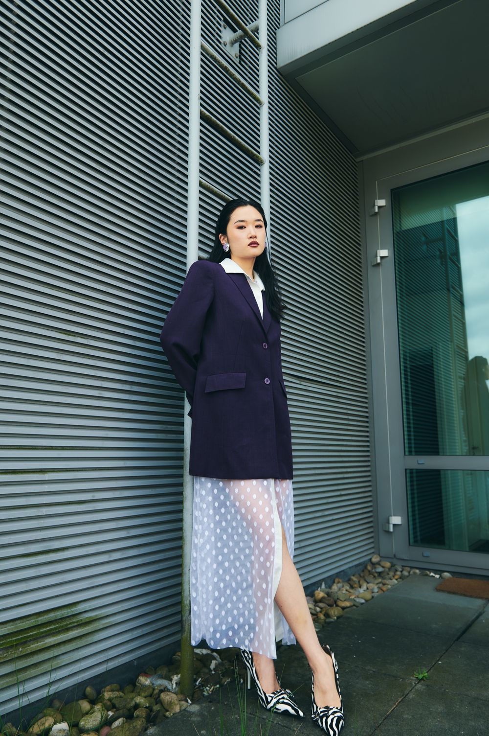 A person in a navy cardigan and polka dot dress poses against a corrugated metal wall in multiple fashion shots.