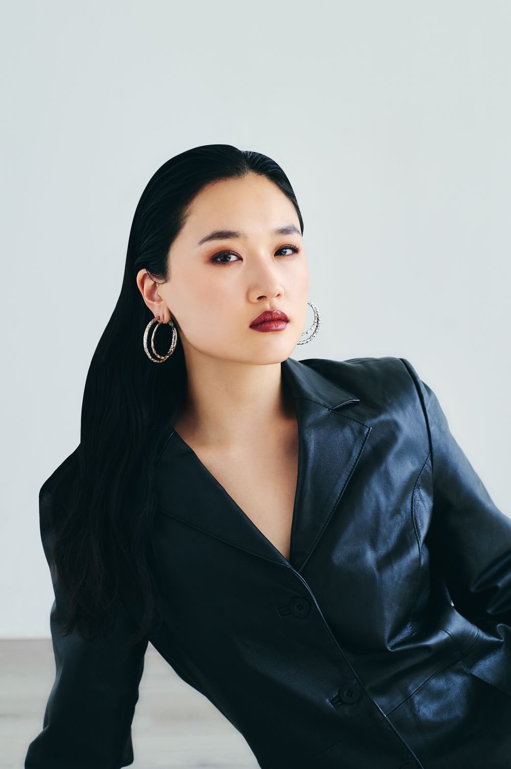 Fashion portrait of a model wearing a black blazer against a light background in a minimalist studio setting.