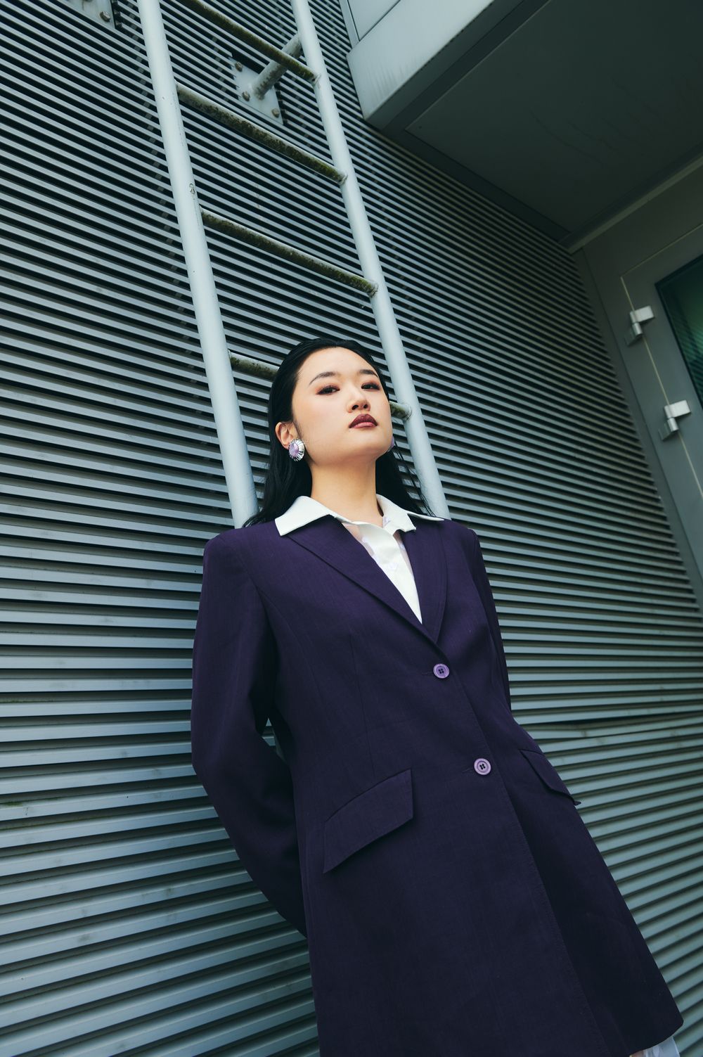 Professional wearing a dark business suit stands against modern architectural lines and metallic background.