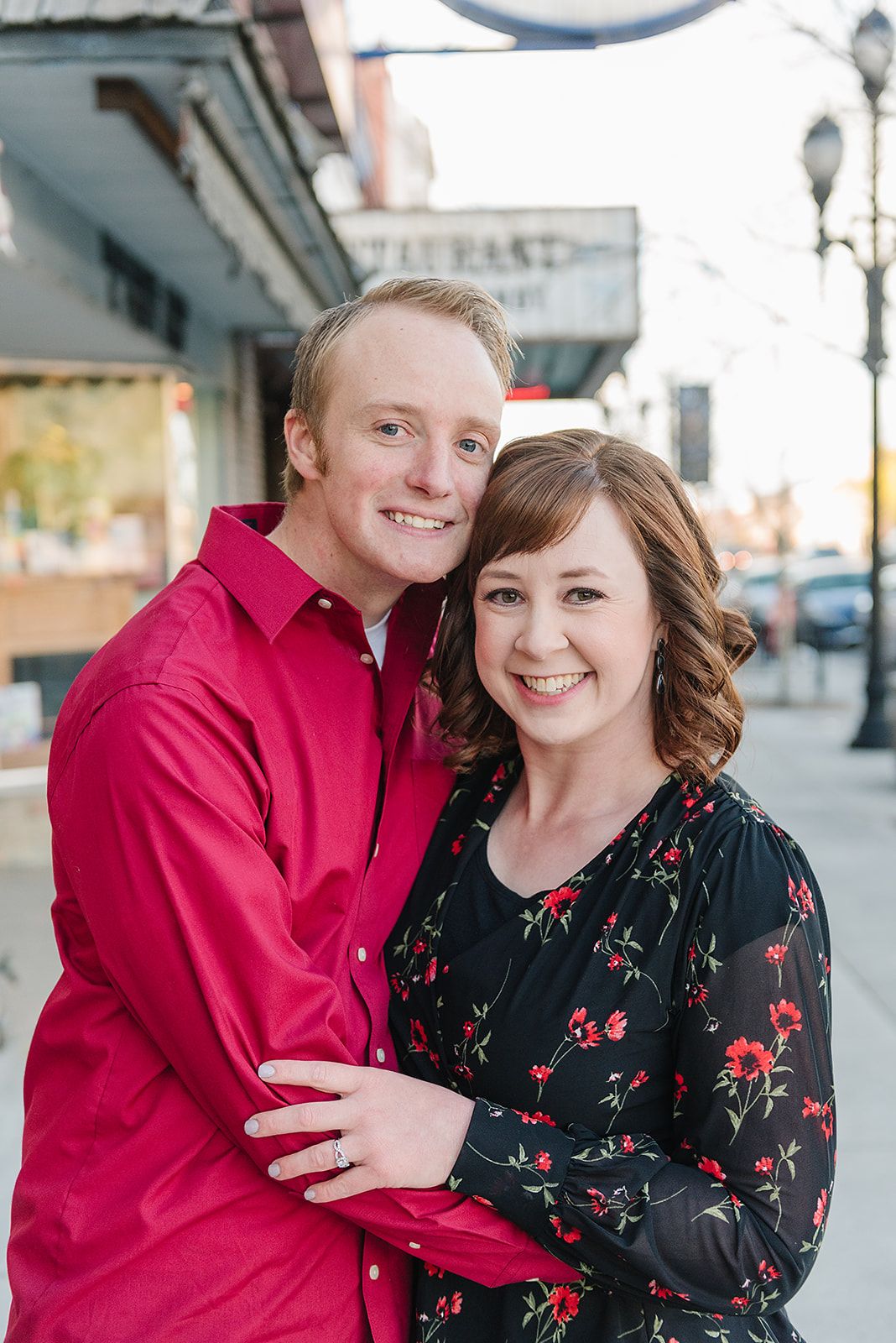A couple poses together in downtown, wearing festive red and black outfits.