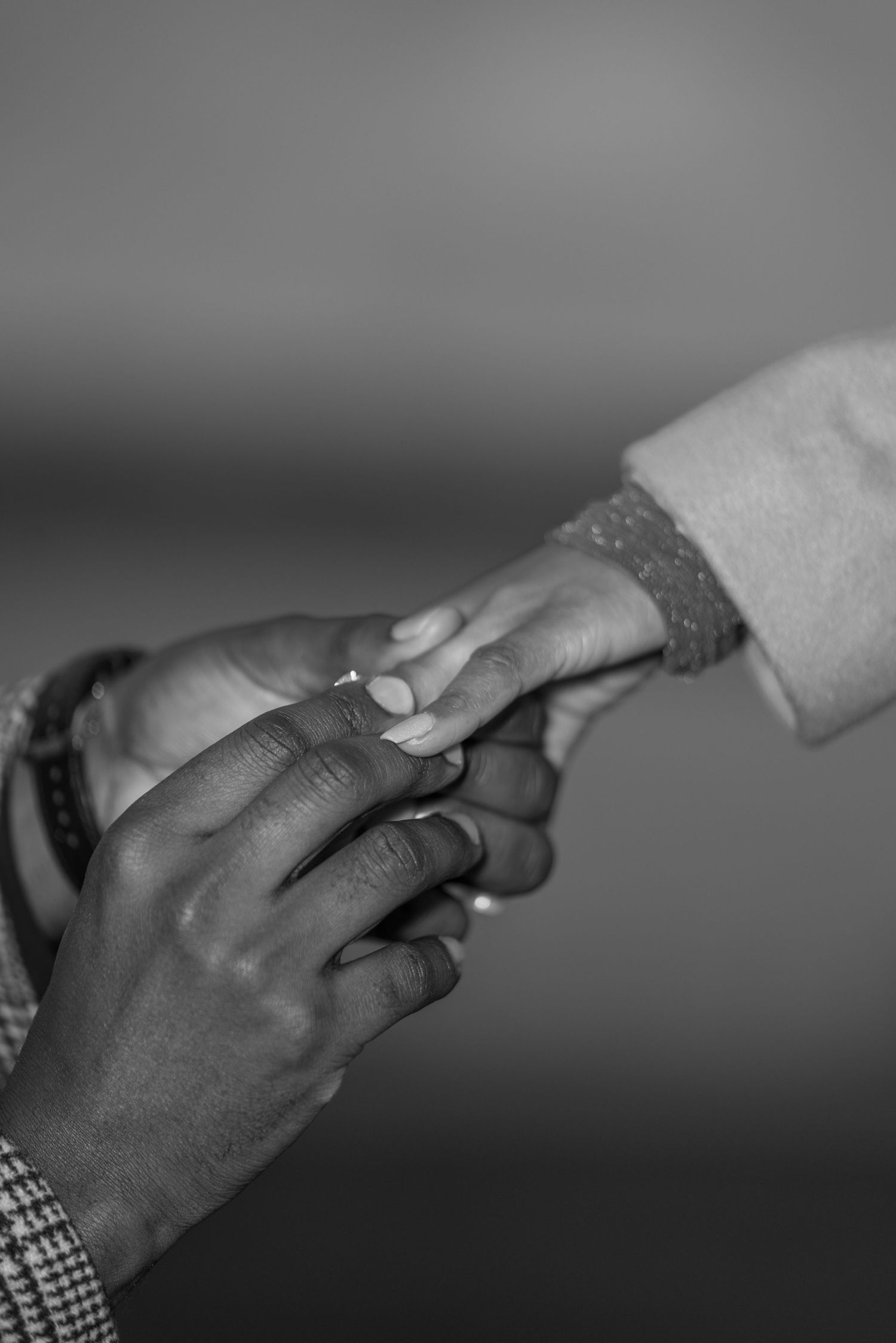A close-up black and white photo showing hands exchanging a wedding ring during a proposal or ceremony.