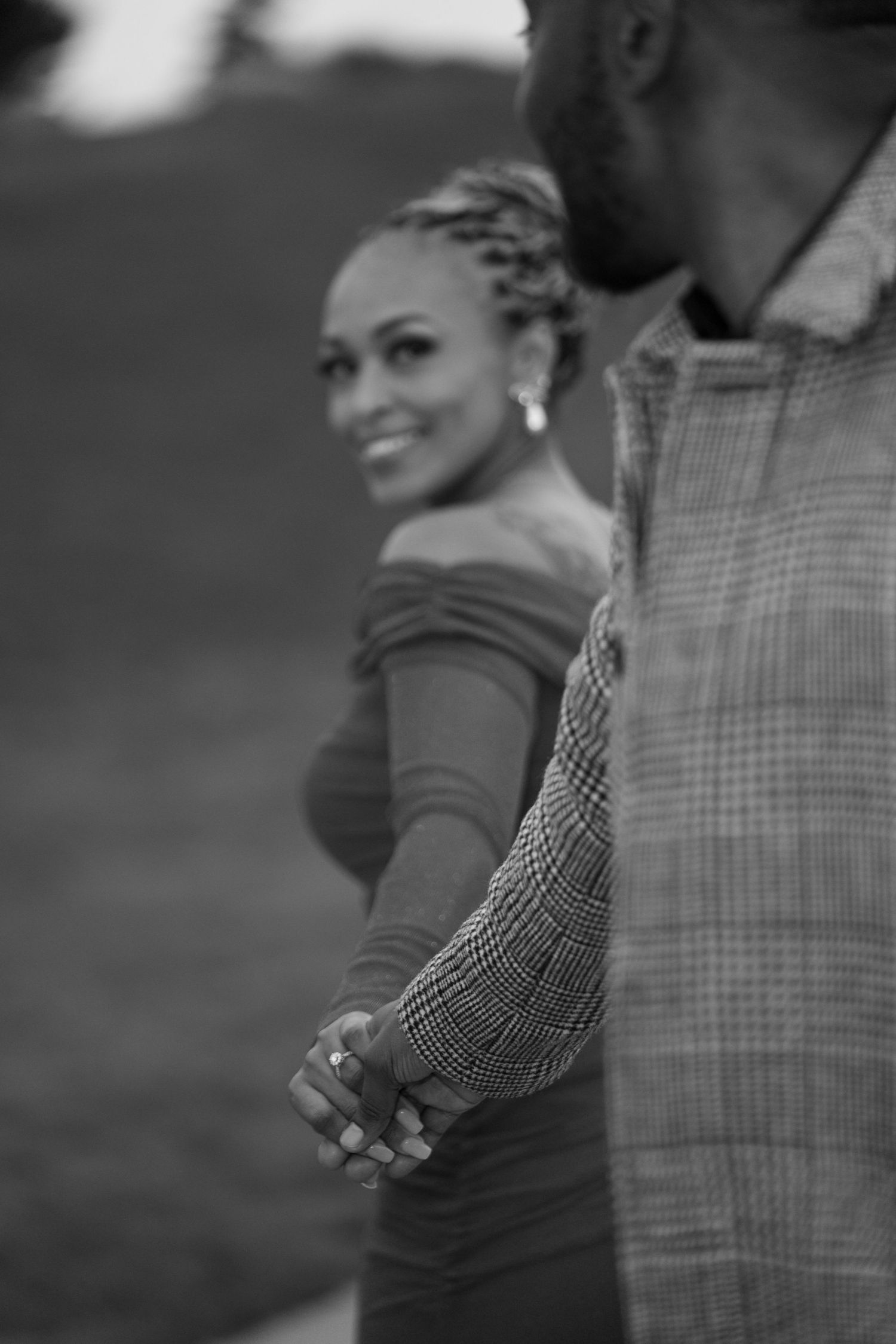 A romantic black and white portrait shows a couple holding hands and sharing a tender moment outdoors.