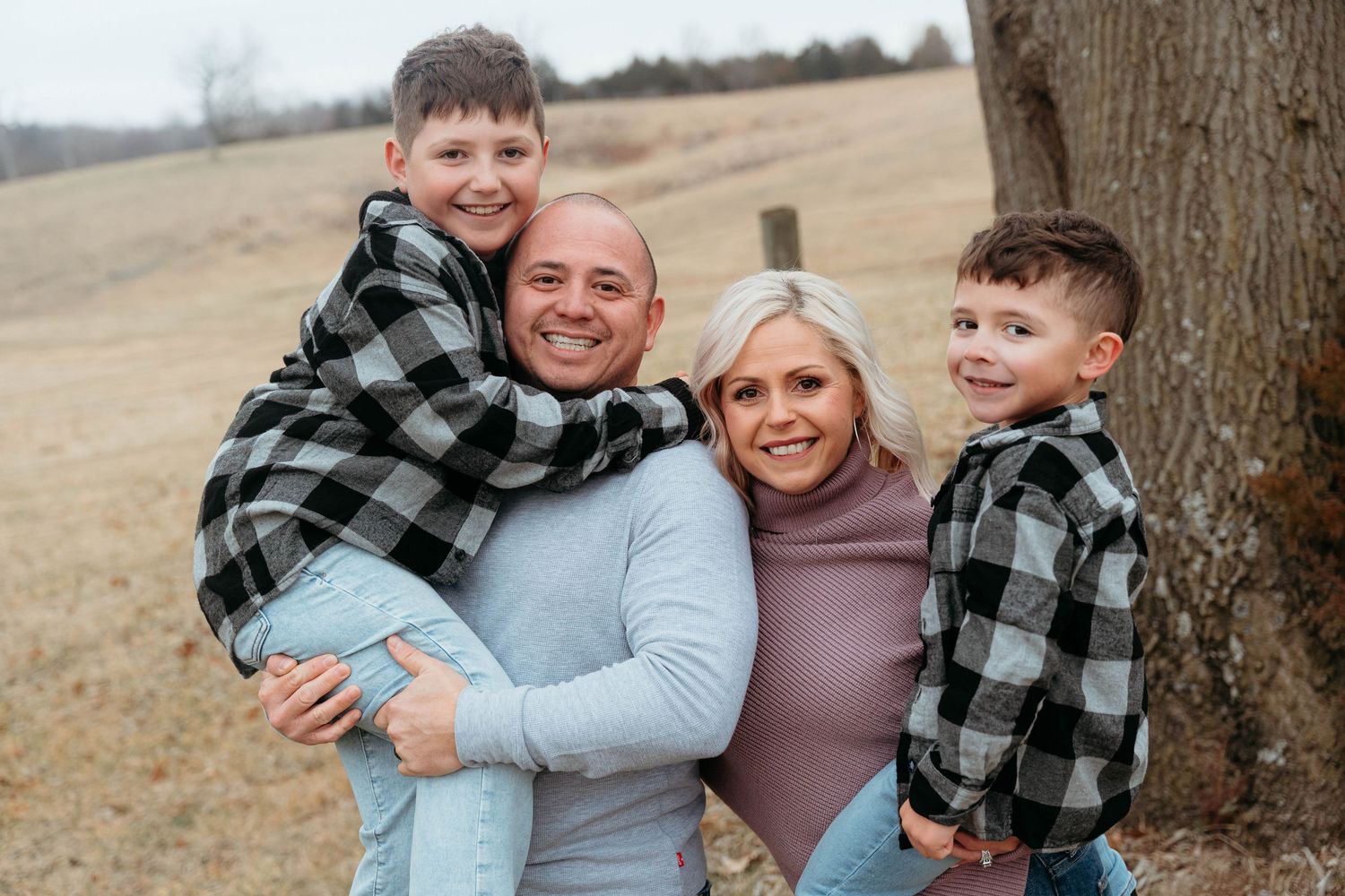 A casual outdoor family photoshoot with parents and child wearing plaid and earth tones.