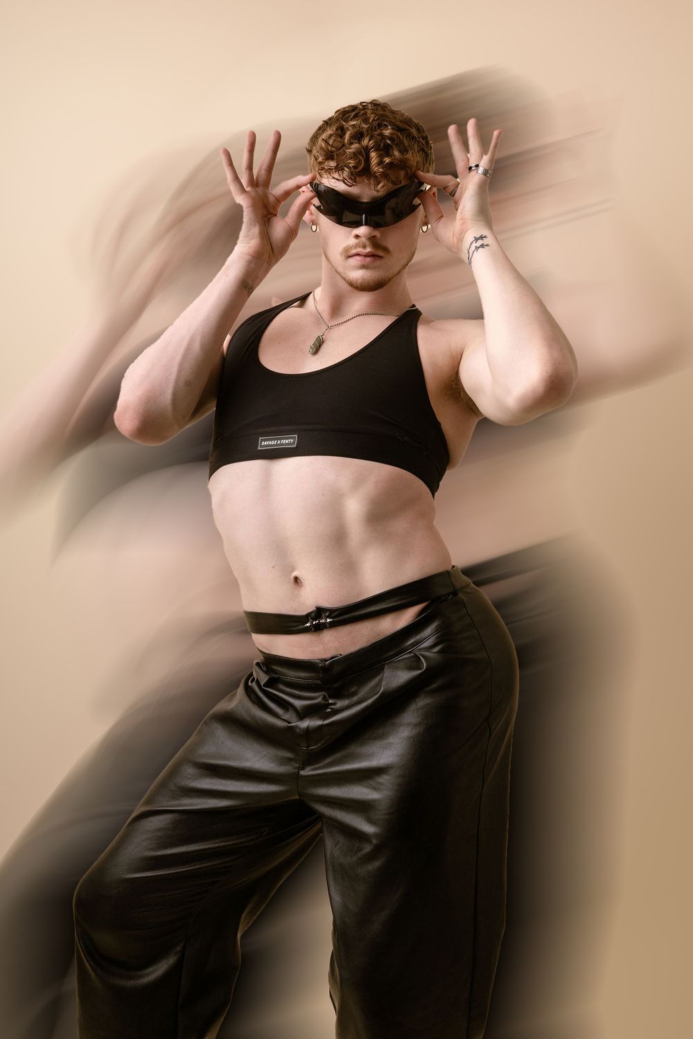 Athletic dancer in black crop top and dark pants strikes dramatic pose against beige background with motion blur effect.