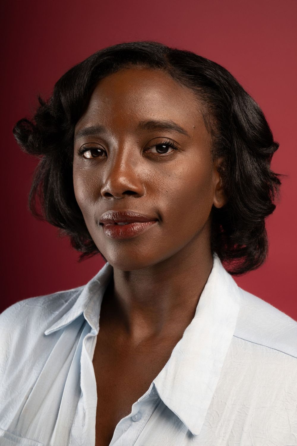 Professional studio portrait of someone wearing a white button-up shirt against a burgundy background.
