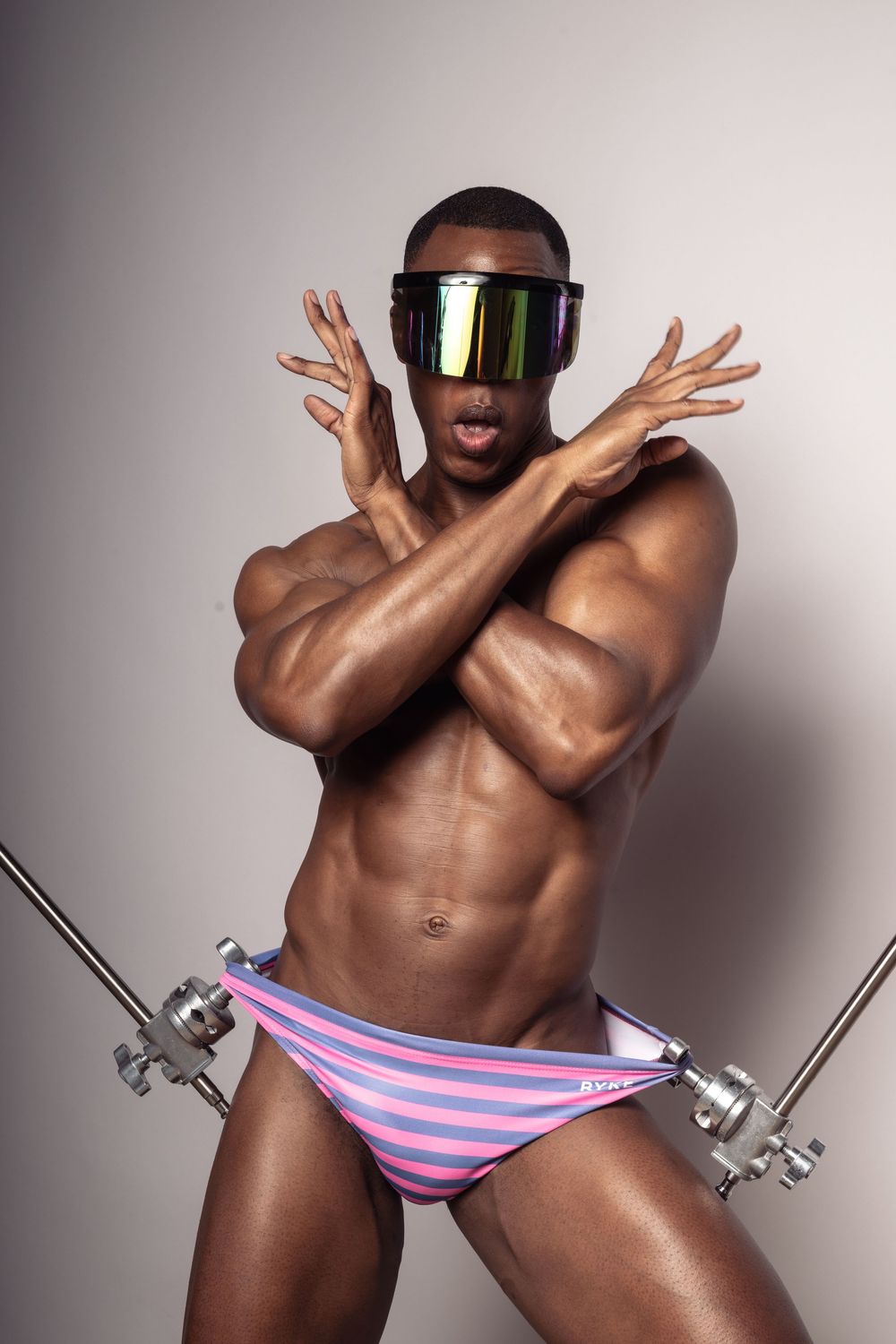 Muscular figure wearing futuristic visor and striped swimwear poses with crossed arms.